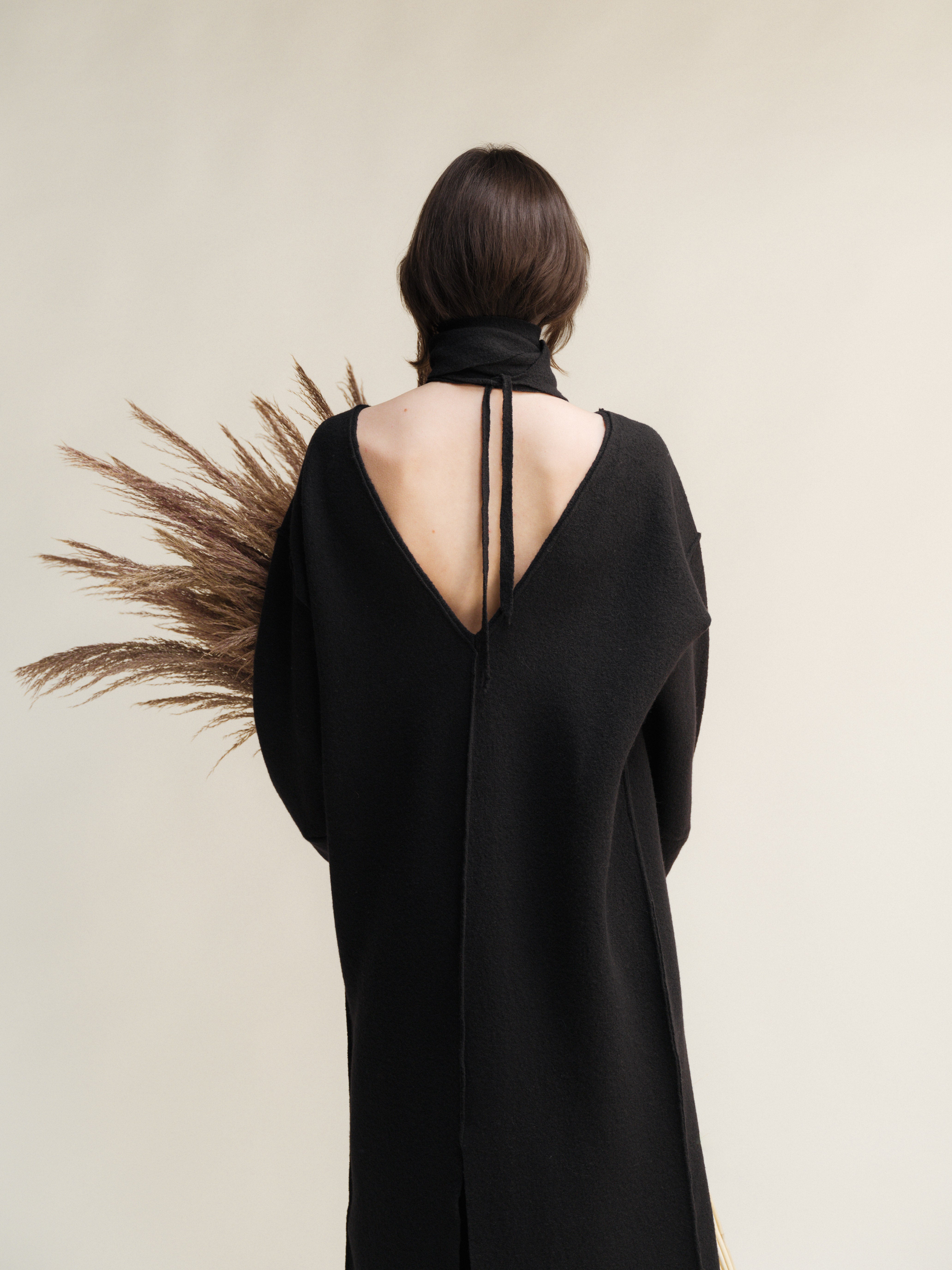 Person wearing a black dress with a deep back cut, standing against a neutral background.