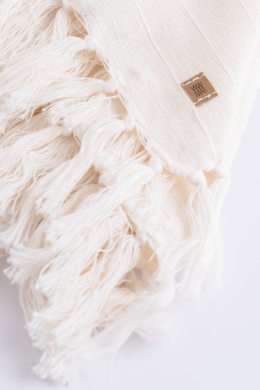 White blanket with tassels on a light gray background