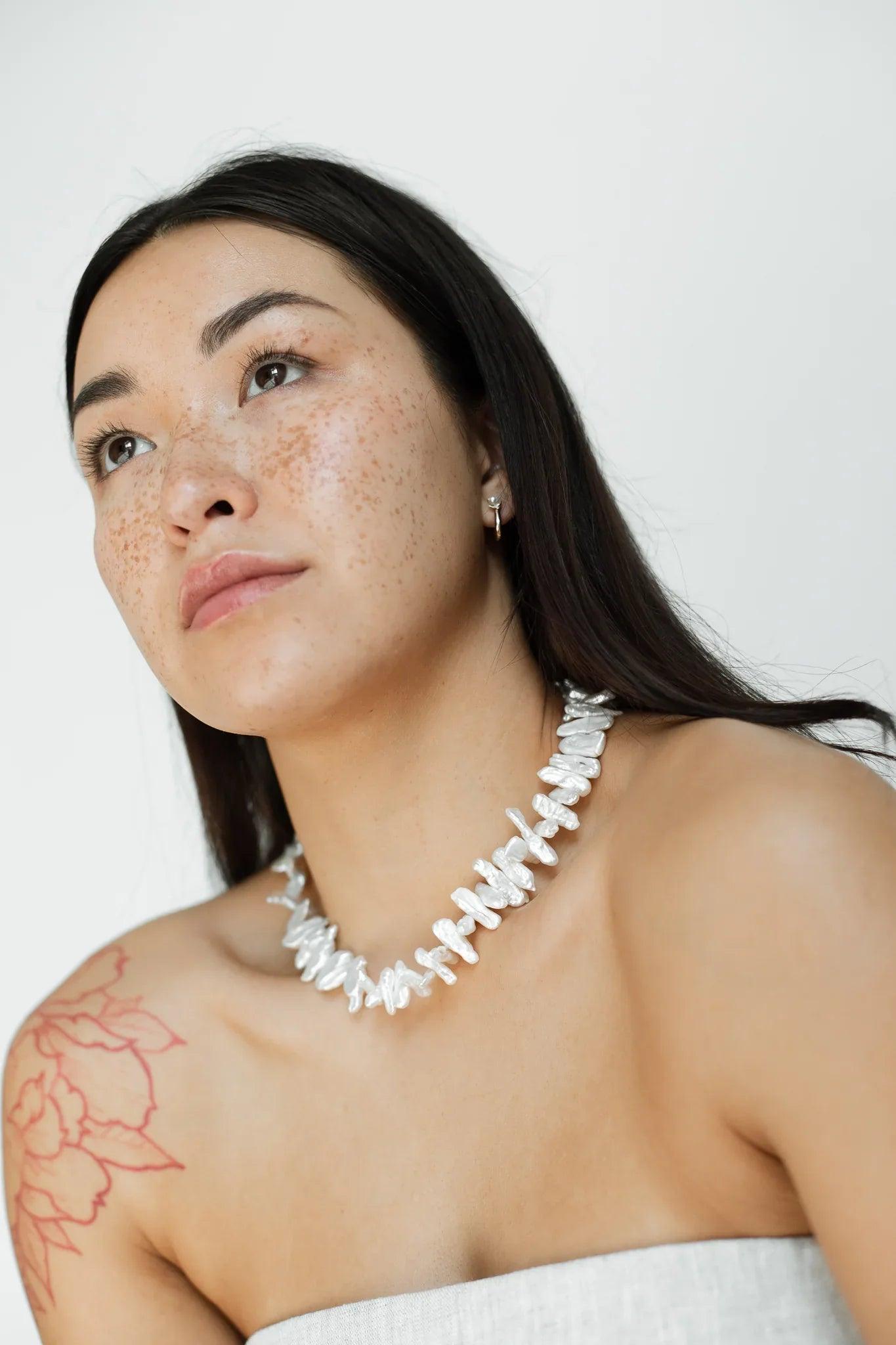 Woman wearing a white necklace against a plain background