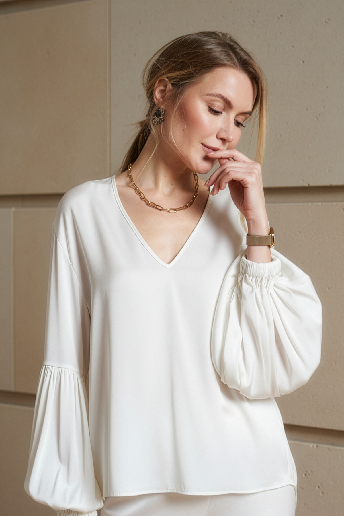 Woman wearing a white blouse with balloon sleeves against a beige wall.