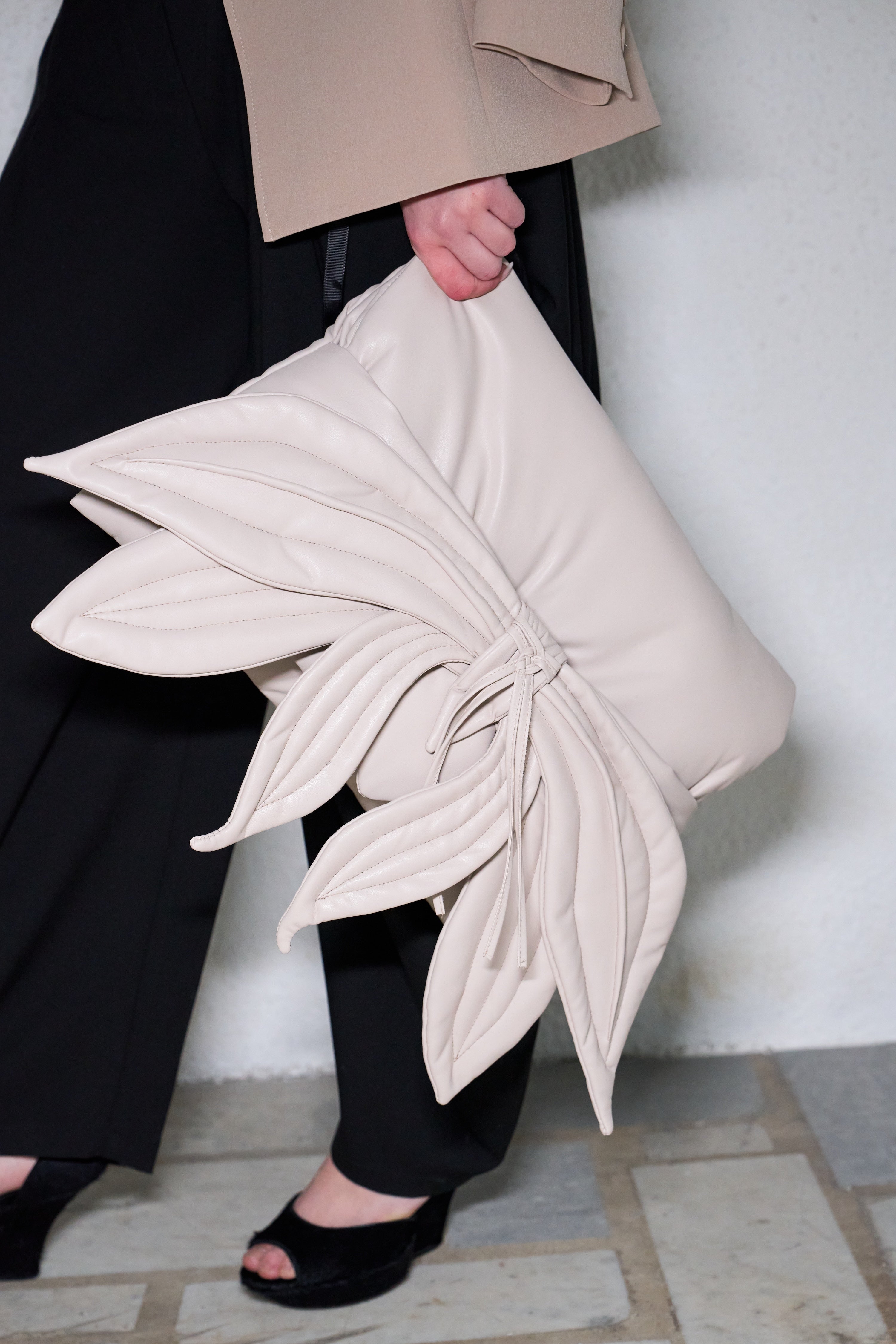 Person holding a large beige clutch with leaf-like design against a neutral background