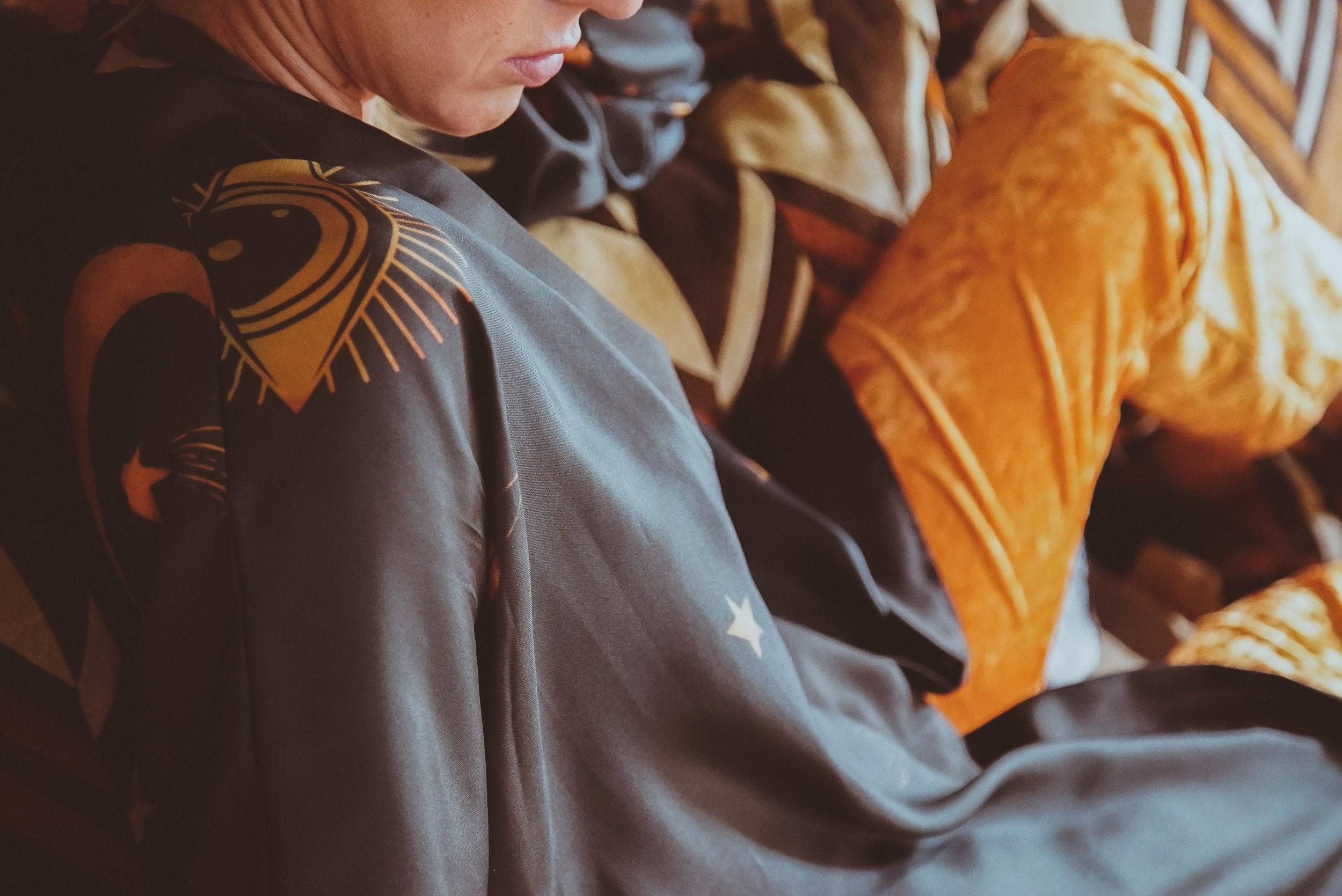 Person wearing a dark robe with a gold emblem, sitting on a chair.