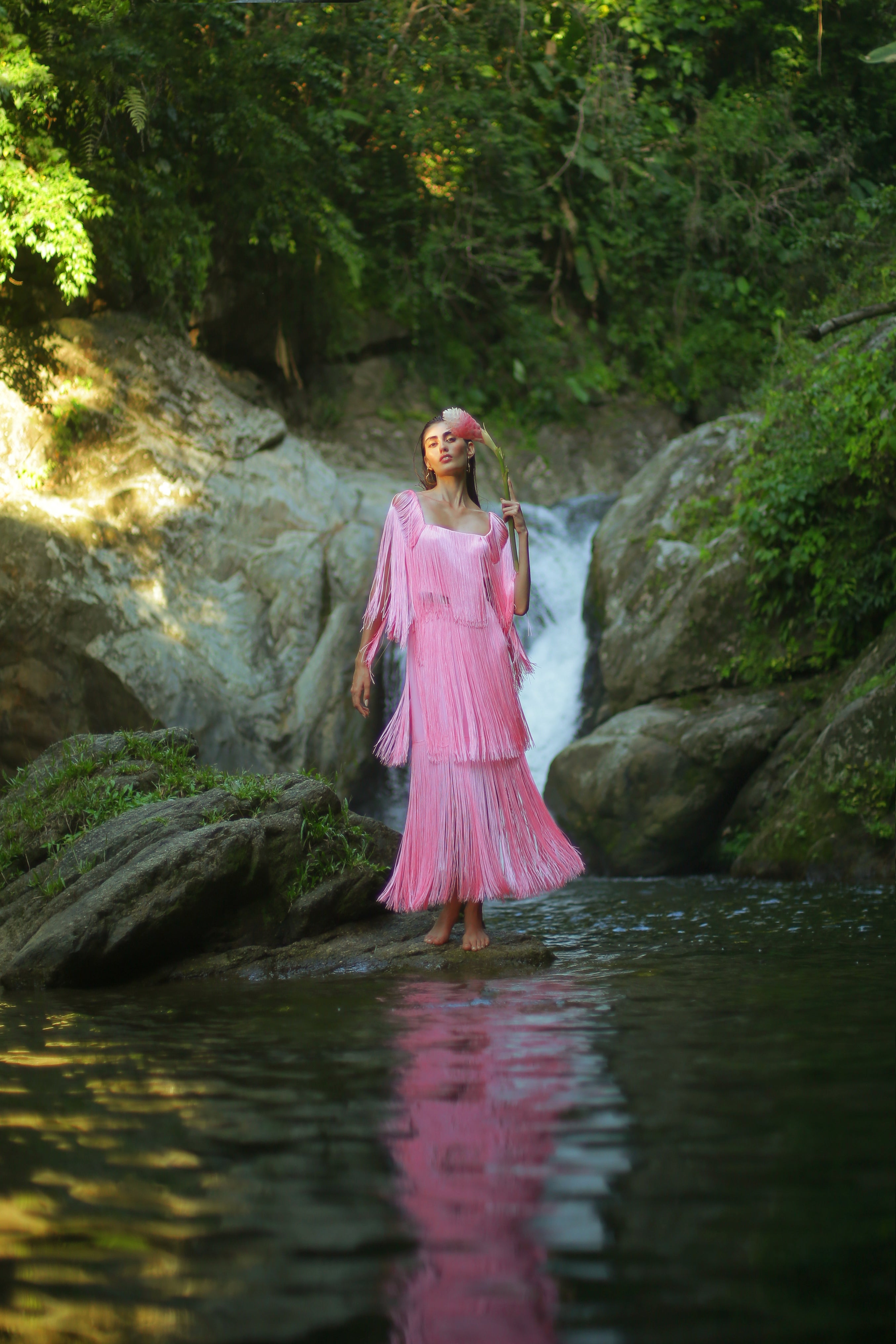 Woman in a pink dress standing by a waterfall with greenery around