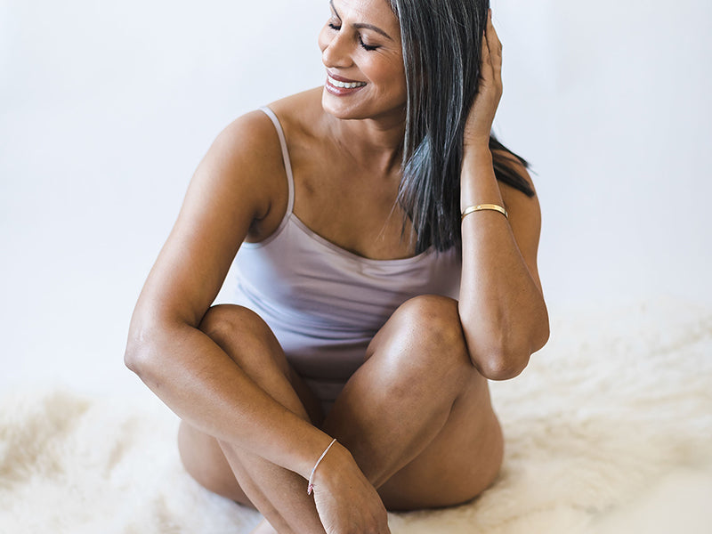 Woman sitting on a white surface wearing a light pink tank top.