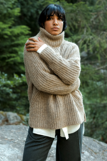 Person wearing a large beige knitted sweater in a forest setting