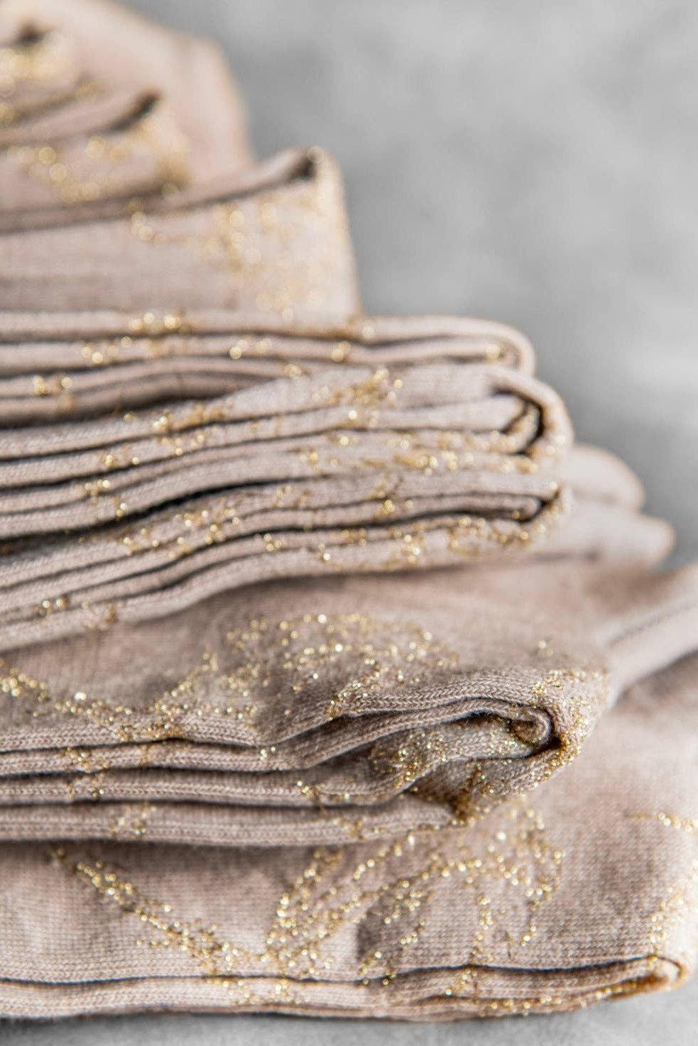 Stack of beige socks with gold speckles on a gray background.
