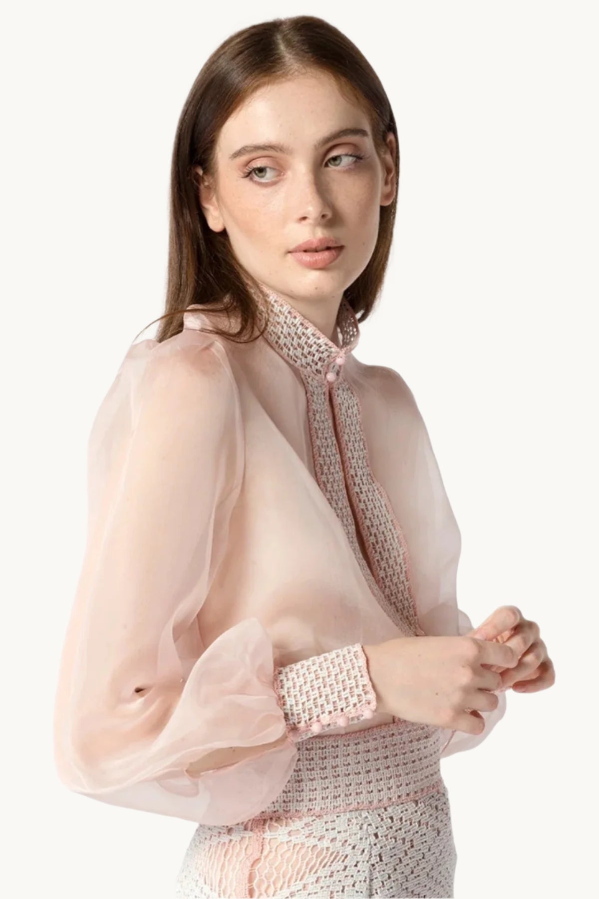 A woman wearing a floral silk organza shirt in pink with crochet detailing.