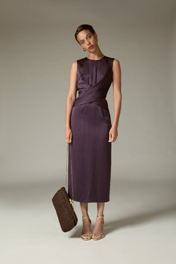Woman in a purple dress holding a matching clutch against a neutral background | Exclude