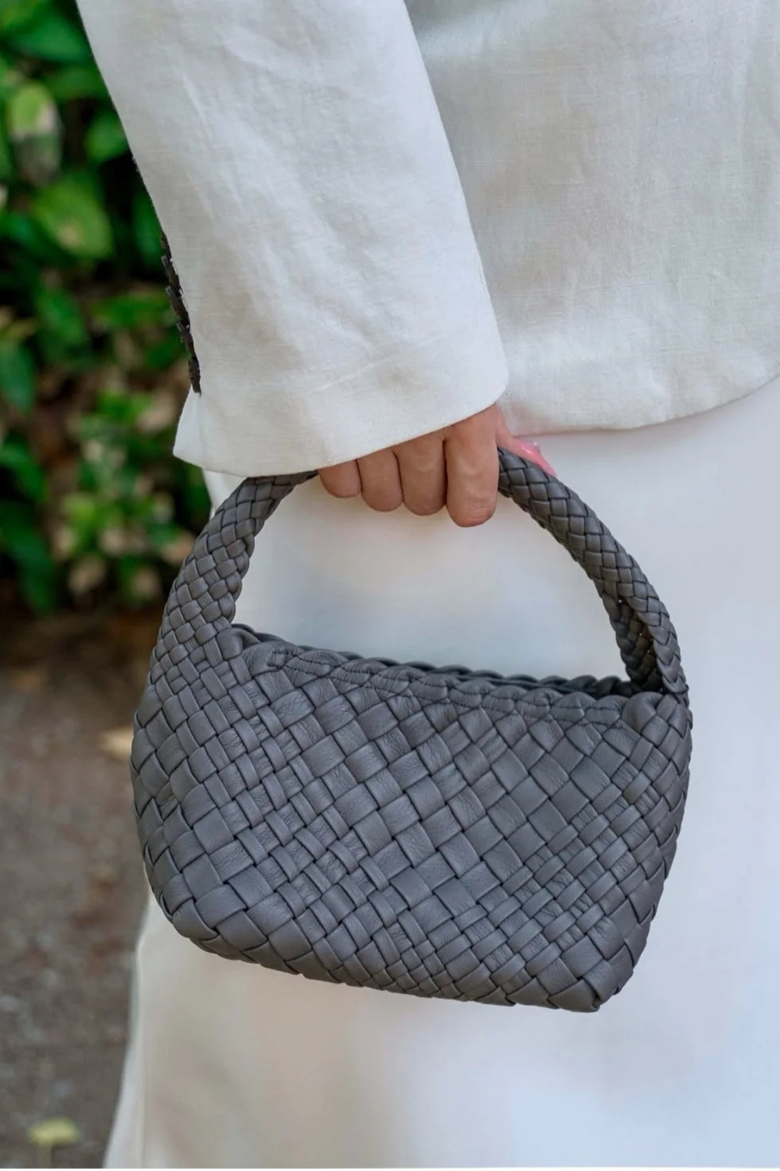 Person holding a woven gray handbag with a blurred green background