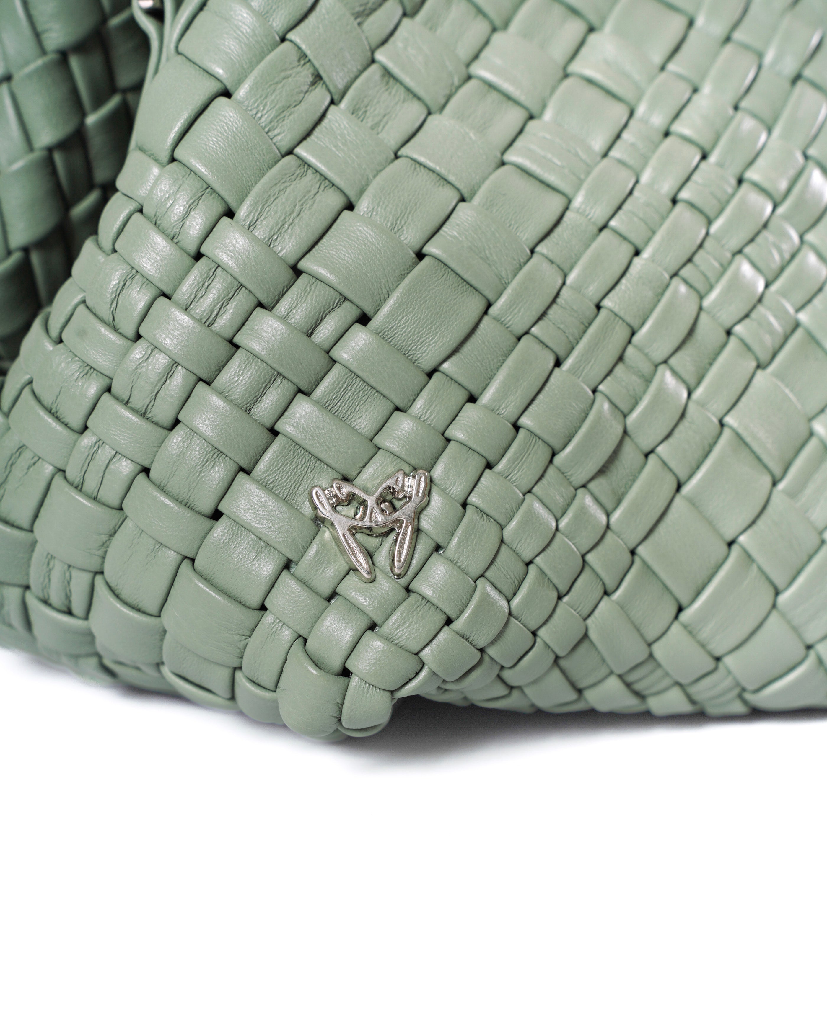 Close-up of a green woven handbag with a decorative clasp on a white background