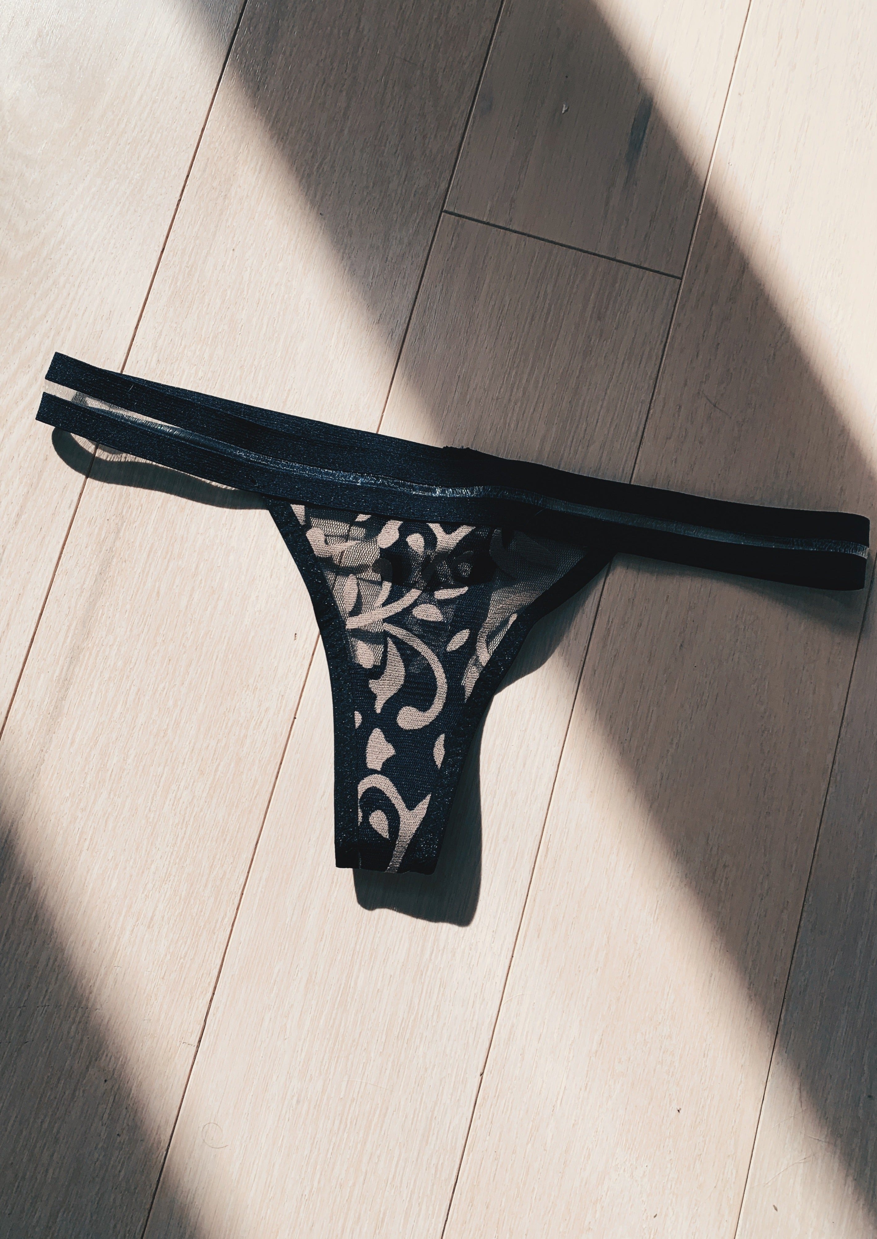 Black thong with floral patterns on a wooden floor