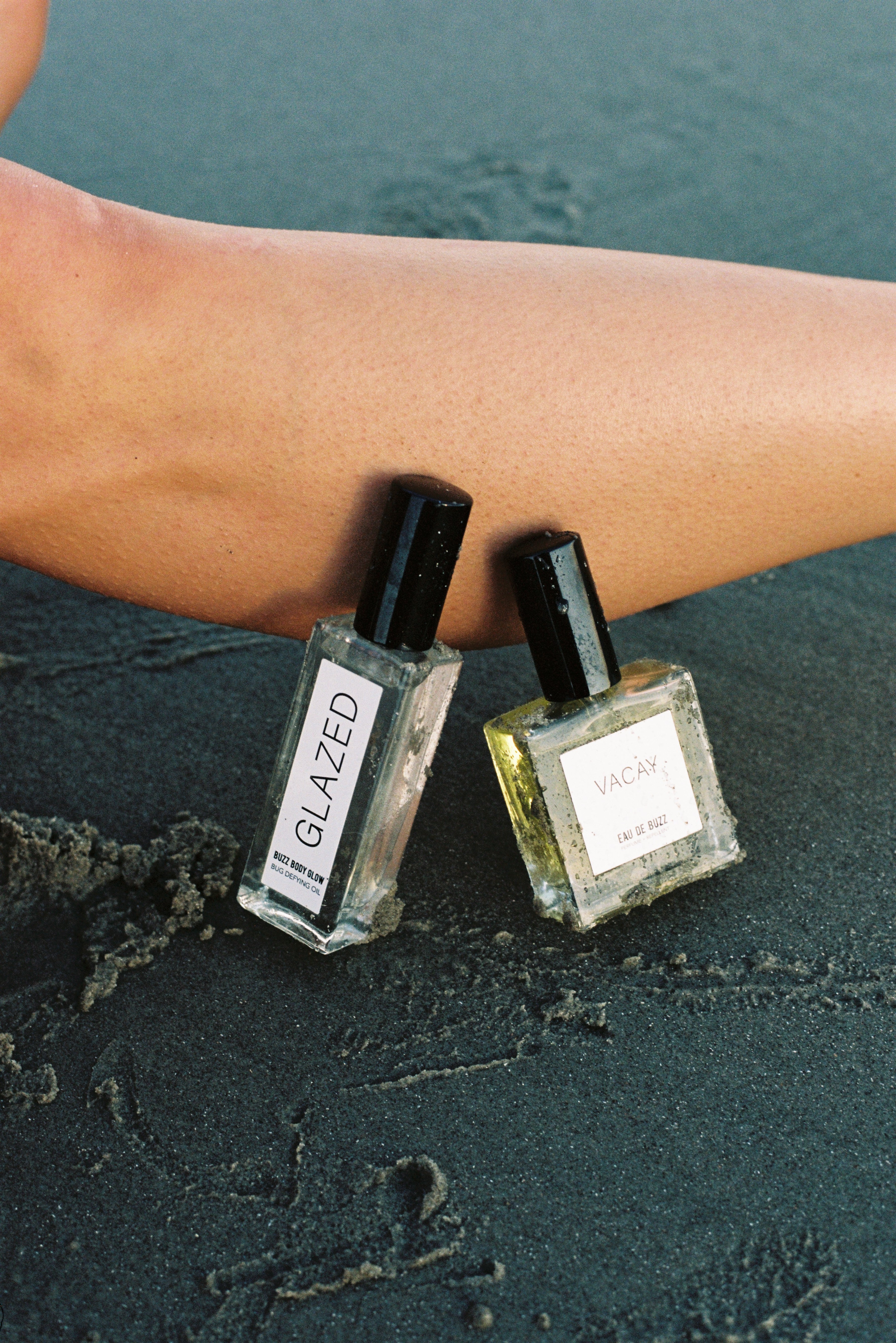Two perfume bottles labeled 'GLAZED' and 'VACAY' on a textured surface.