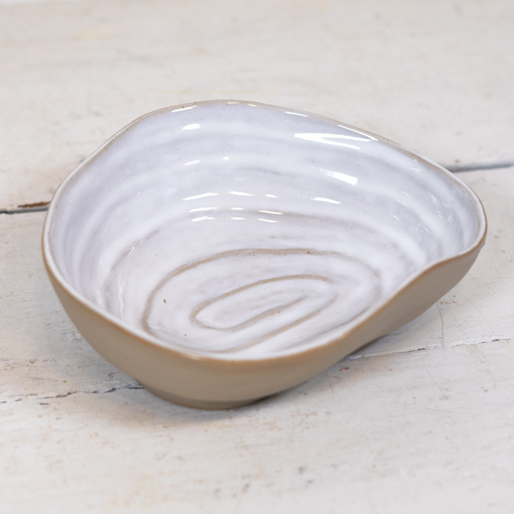 An organic-shaped ceramic dish with a glossy white interior featuring concentric swirl patterns and a matte beige exterior, shown on a light rustic wooden surface.