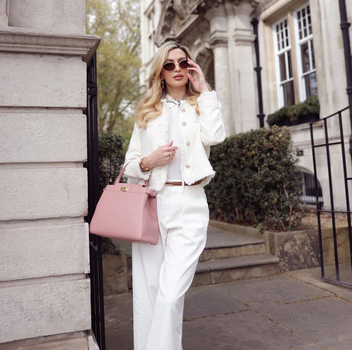Woman in a white outfit with a pink handbag standing outside a building.