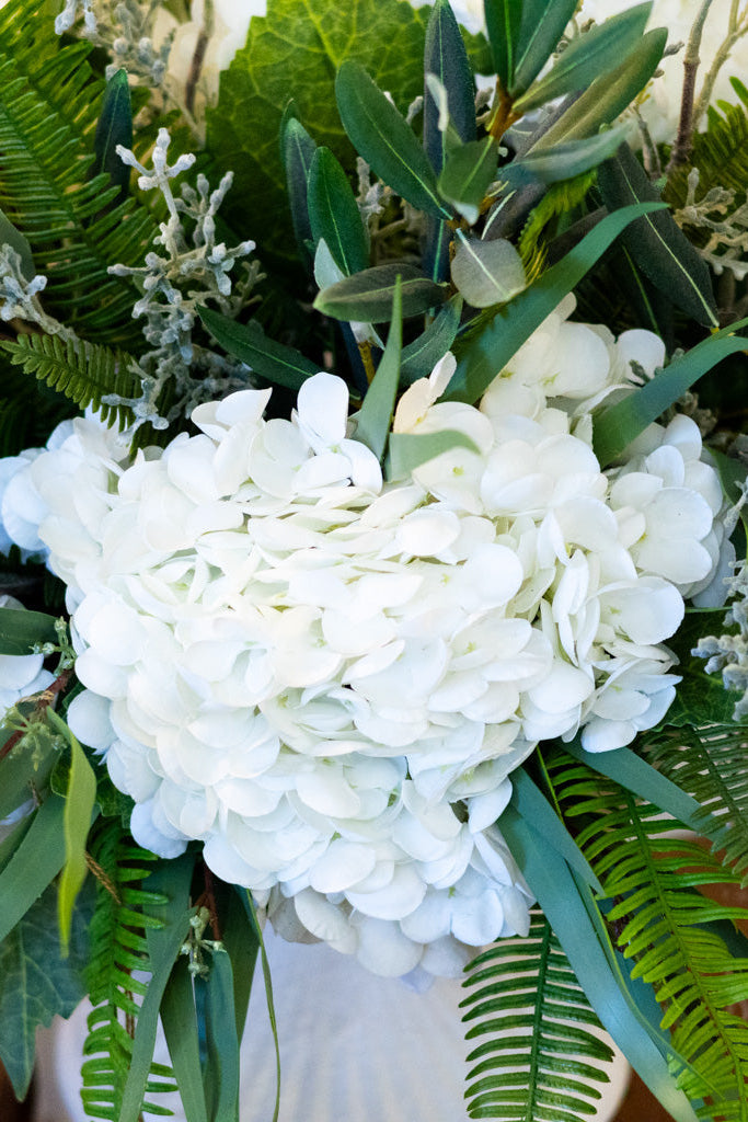 Bouquet of white hydrangeas and greenery in a white vase.