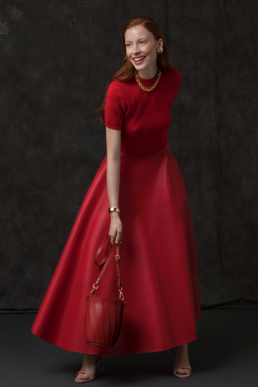 Woman in a red dress holding a matching handbag against a black background