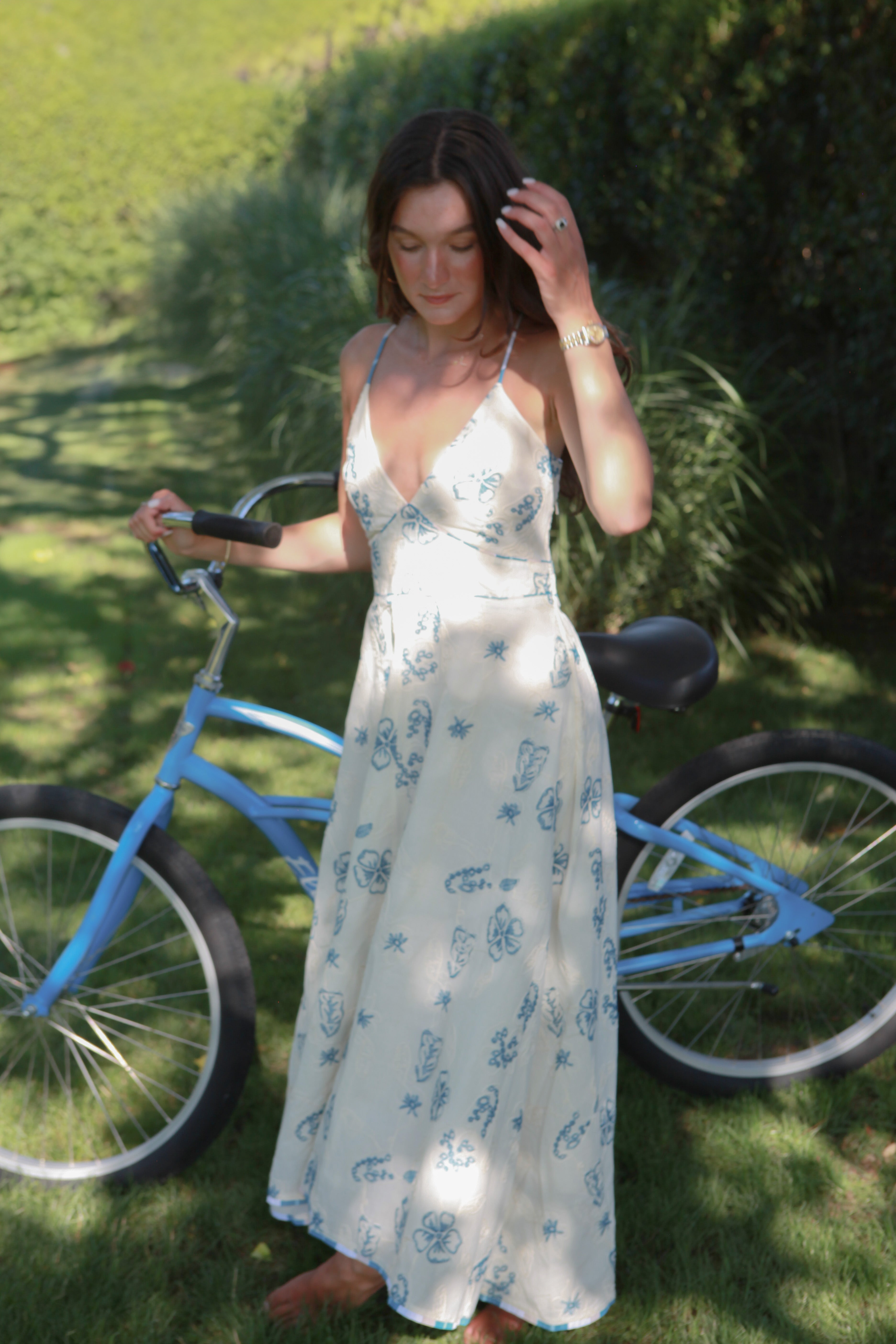 Woman in a white floral dress standing next to a blue bicycle on grass
