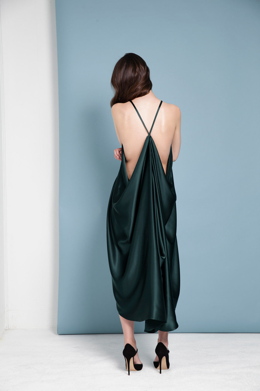 Woman wearing a green silk dress with a backless design against a light blue wall.