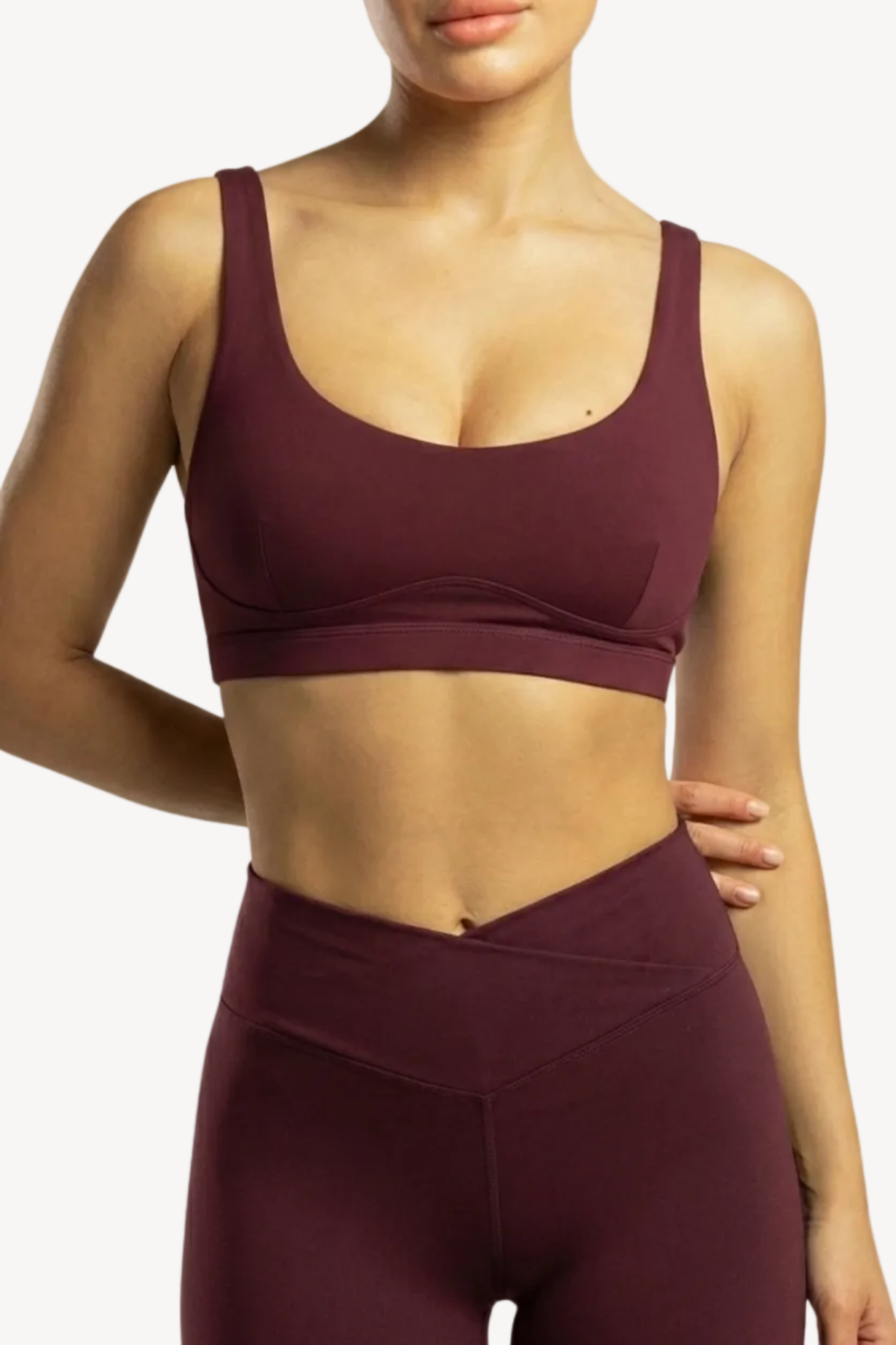 Person wearing a maroon sports bra and leggings on a plain background