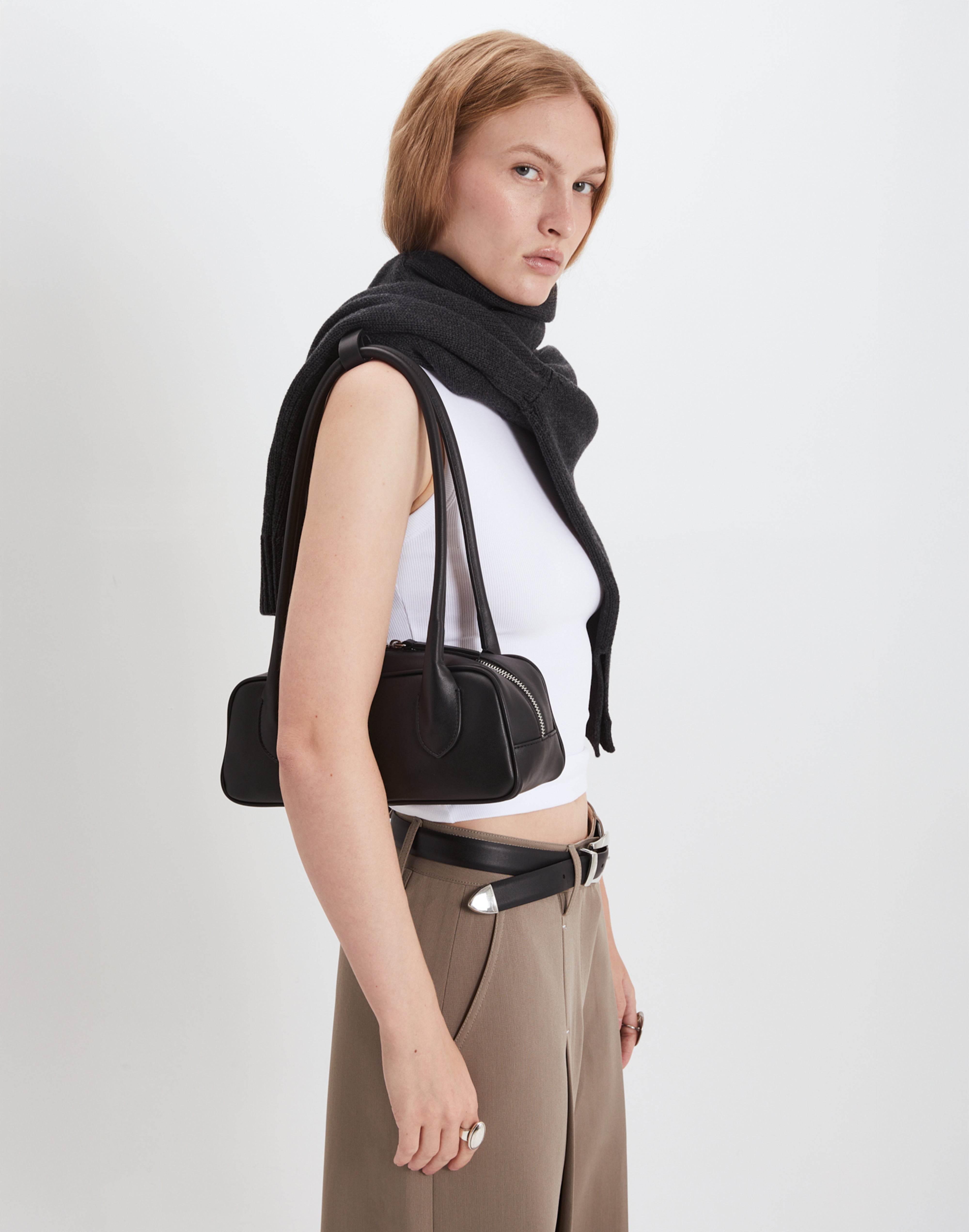 Woman wearing a black scarf, white top, and brown pants with a black handbag on a white background