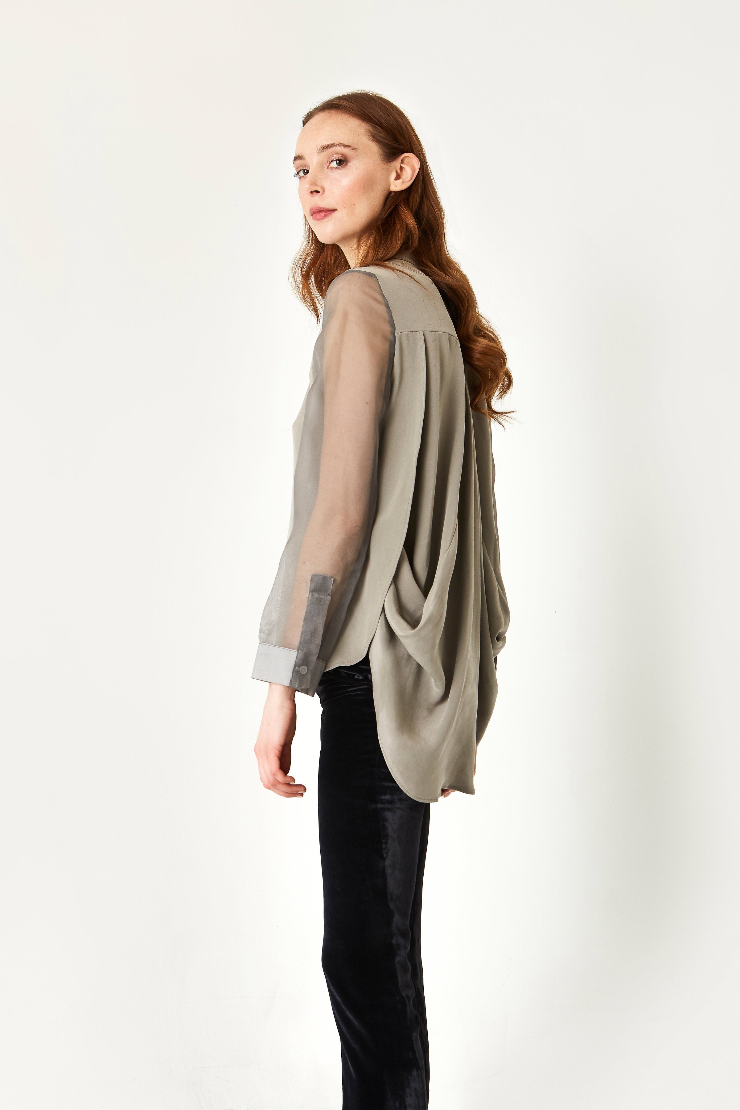 Woman wearing a flowy silver longe-sleeved blouse with a sheer overlay on a white background