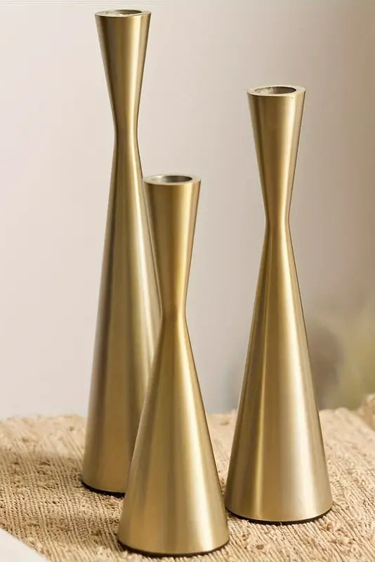 Three gold vases of different heights on a textured surface with a blurred background