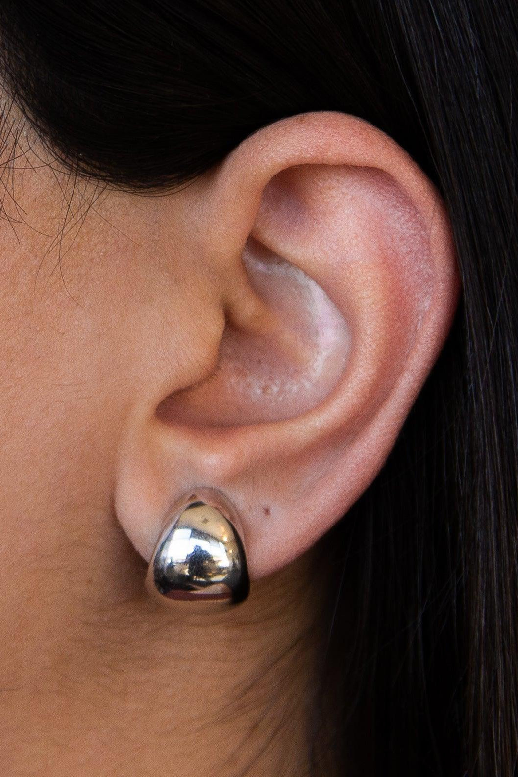 Close-up of an ear wearing a gold heart-shaped earring with dark hair in the background