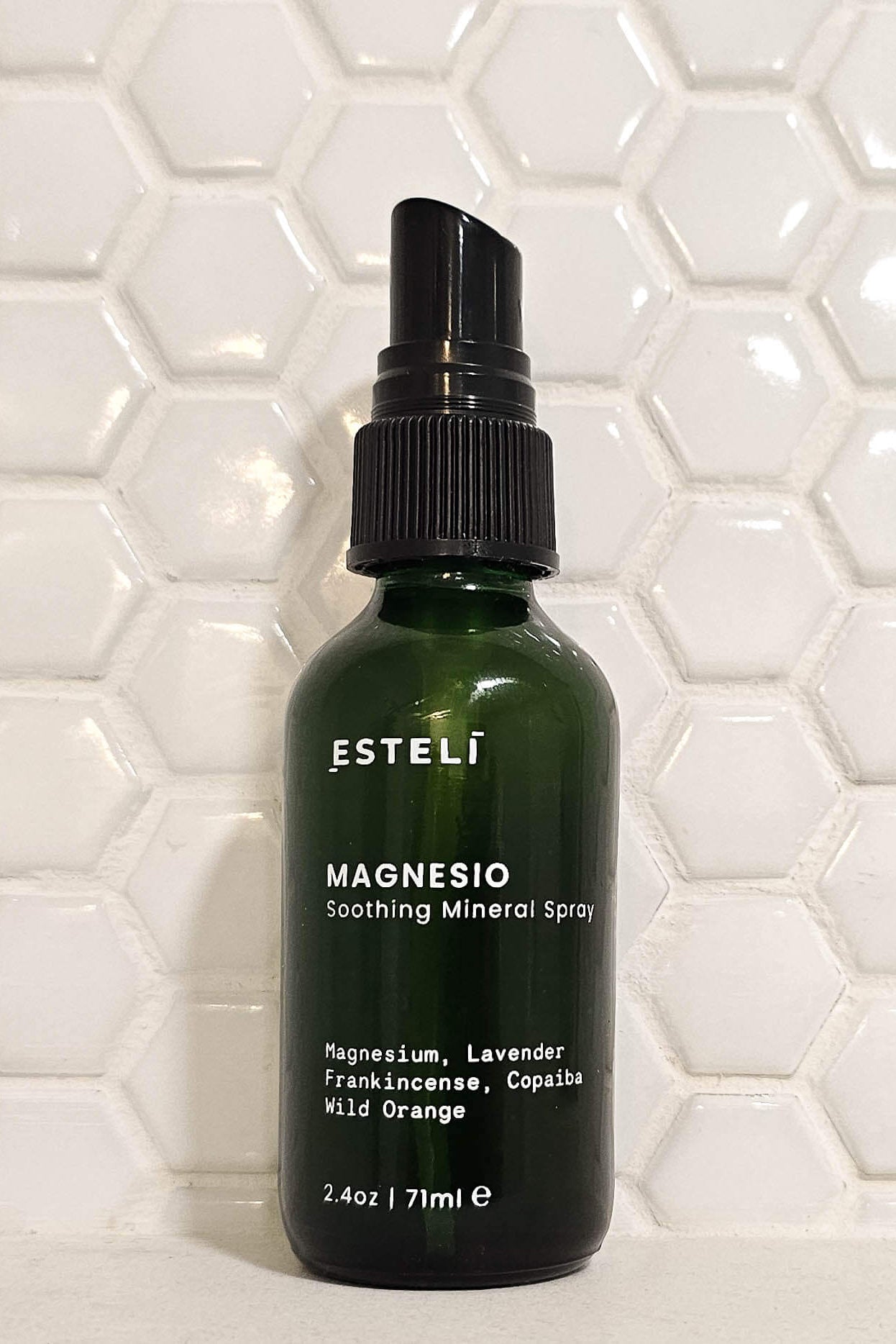 Green spray bottle labeled 'Esteli' on a white tiled wall background