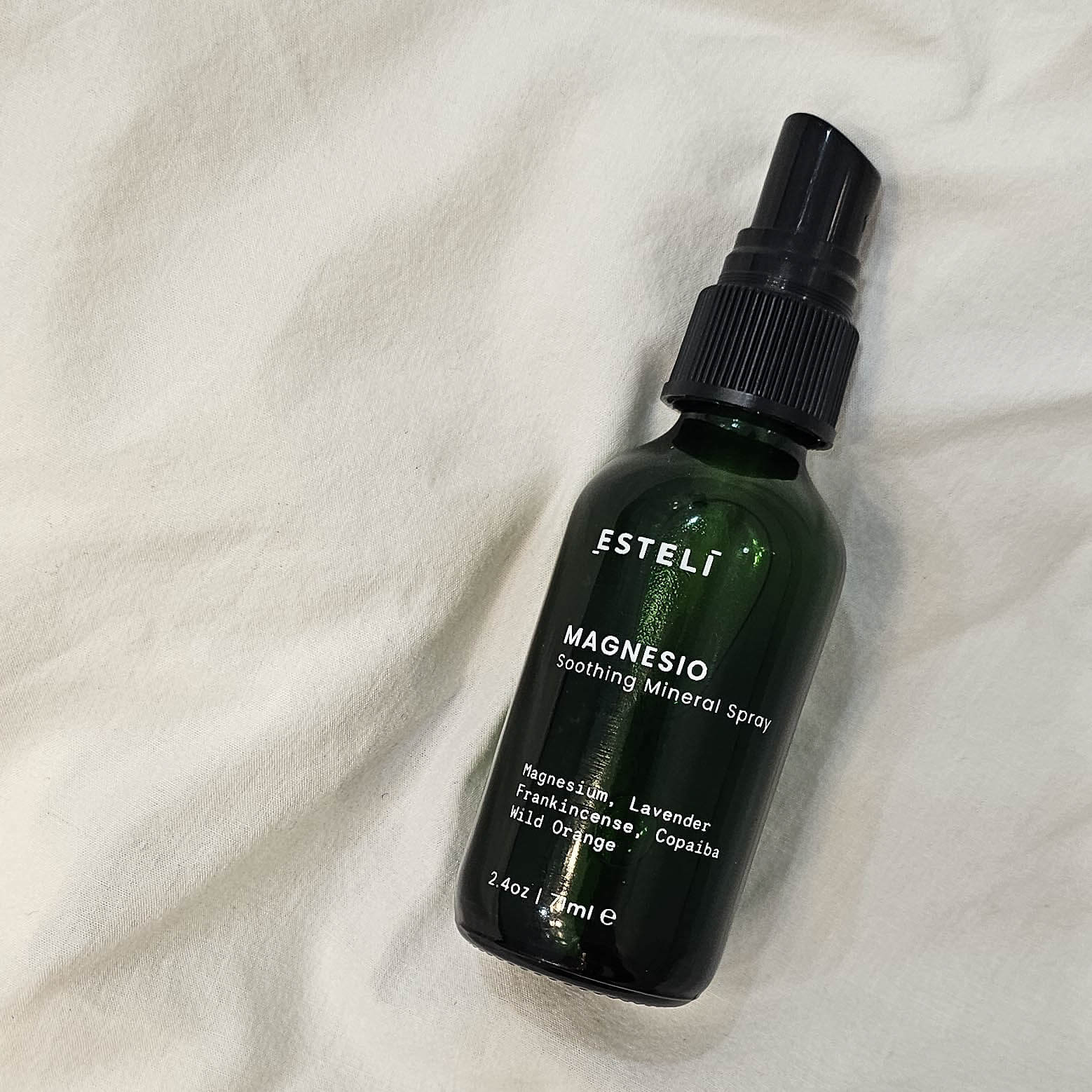 Green bottle of Esteli Magnesio Soothing Mineral Spray on a white fabric background