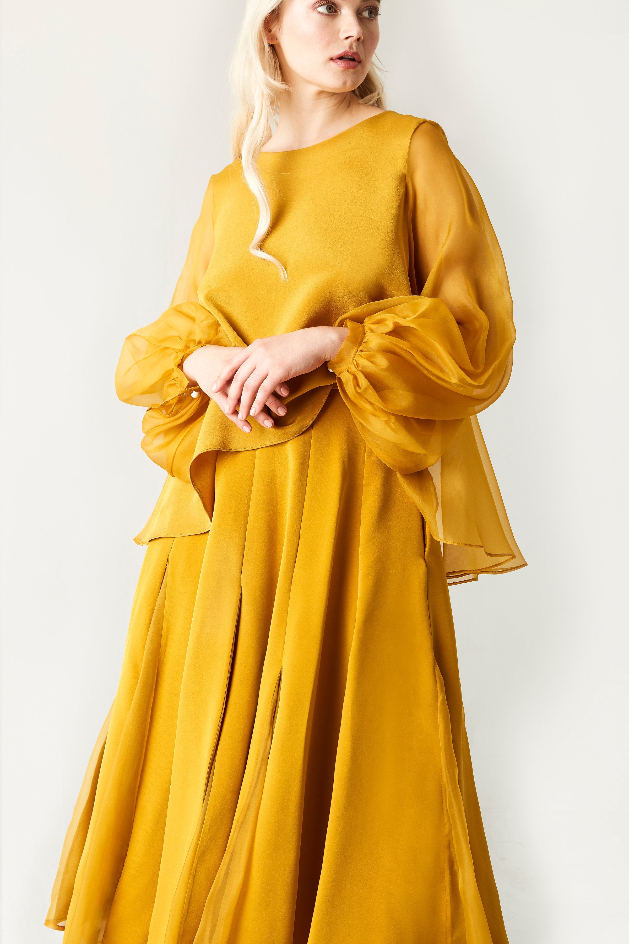 Woman wearing a mustard yellow dress with long sleeves against a white background