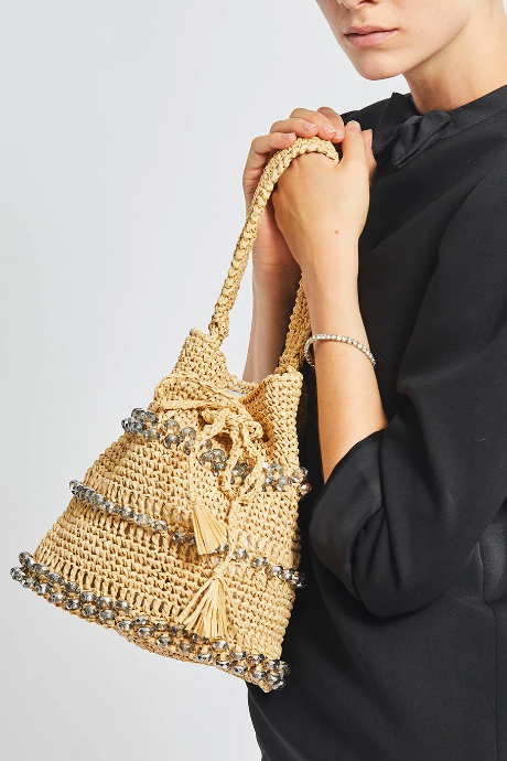 Person holding a woven handbag with decorative elements on a plain background