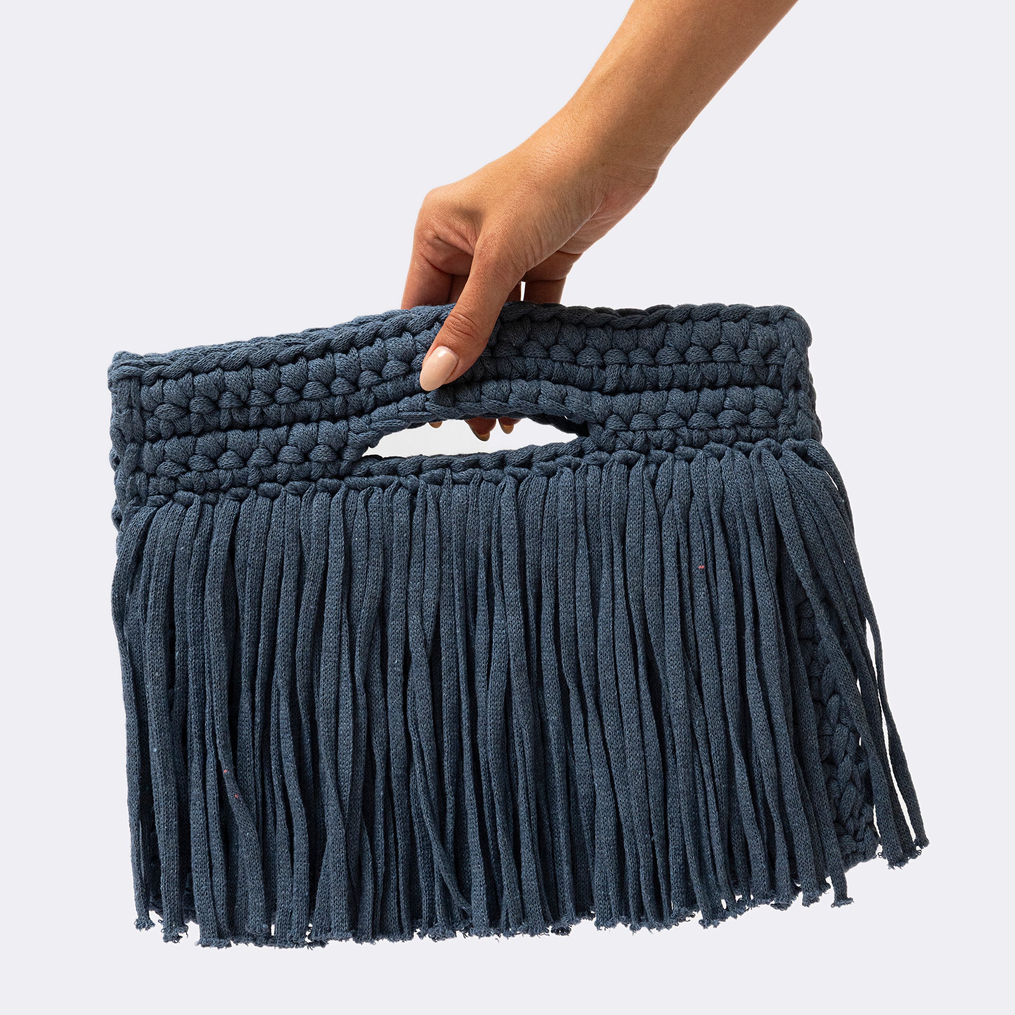 Hand holding a dark blue macrame clutch against a light gray background