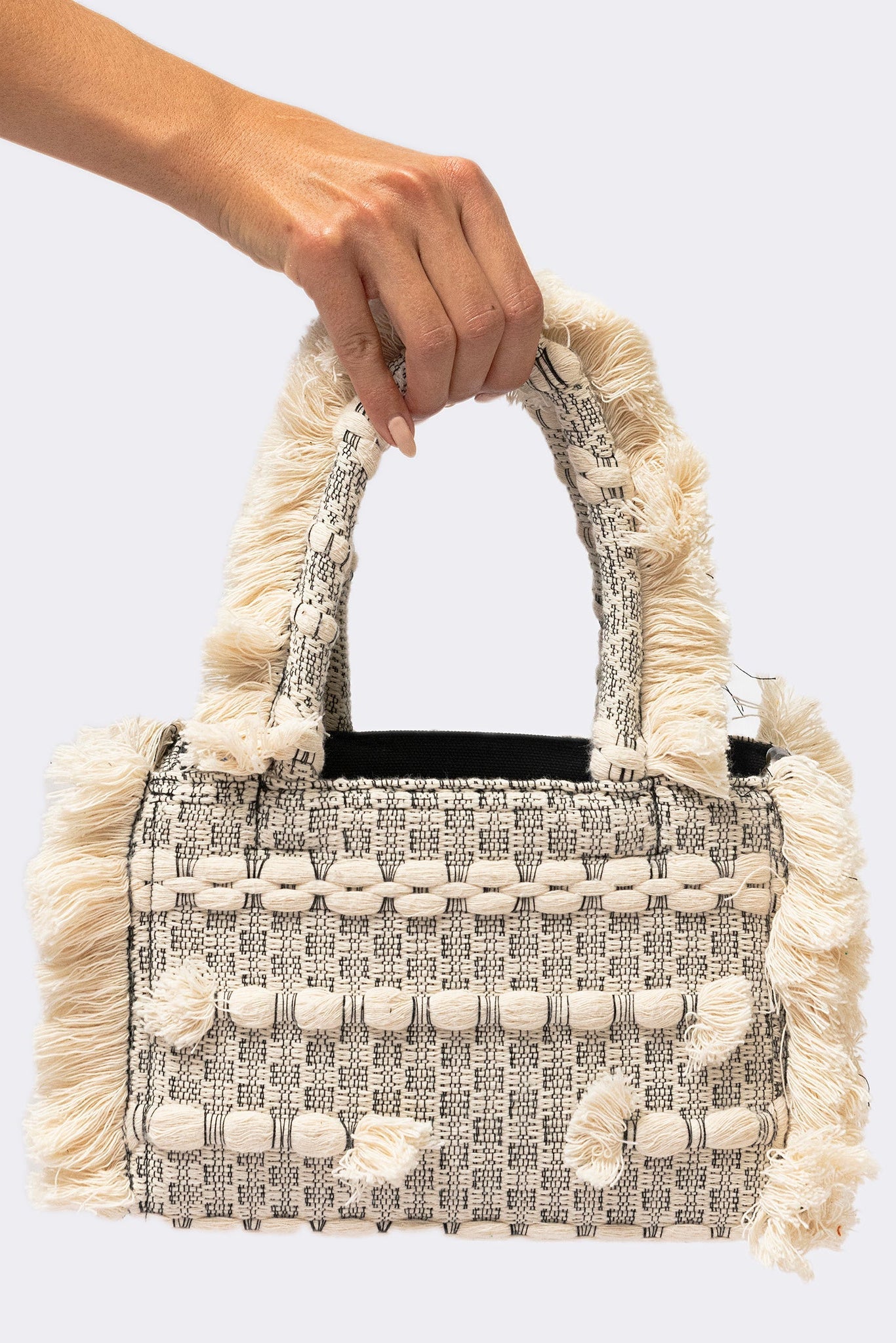 Handbag with decorative fringes held by a hand against a light background