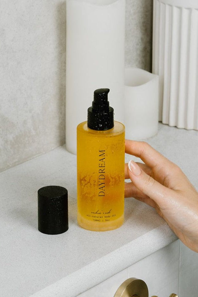 Hand holding a bottle of 'DAVDREAM' body wash on a bathroom counter.