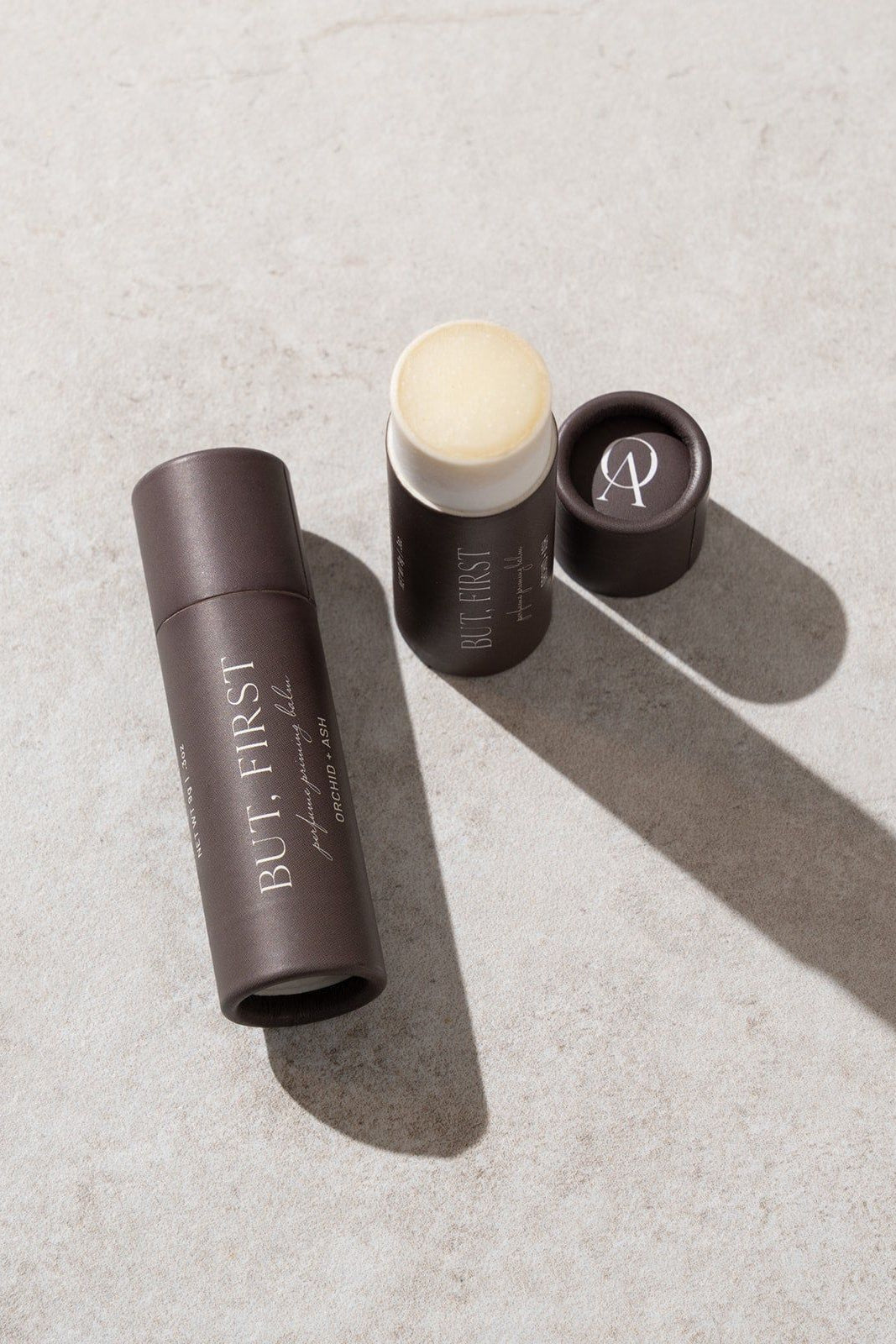 Three cosmetic products on a textured surface with 'But. First.' branding.