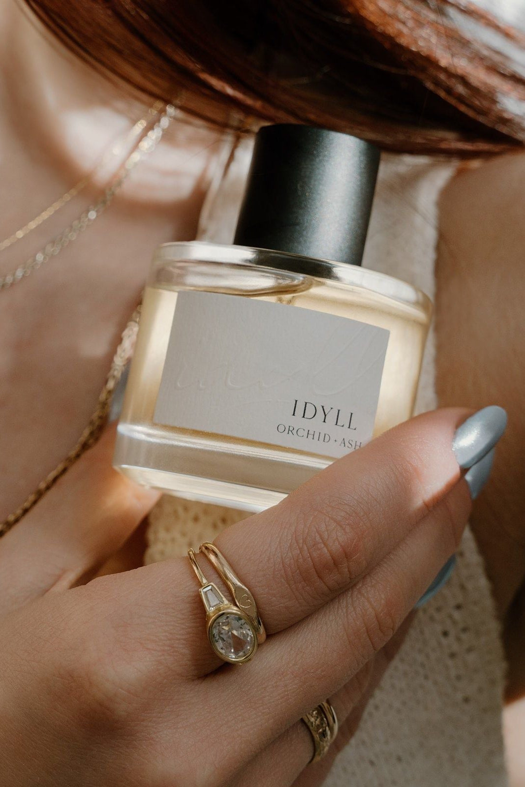 Hand holding a perfume bottle labeled 'IDYLL' with a blurred background