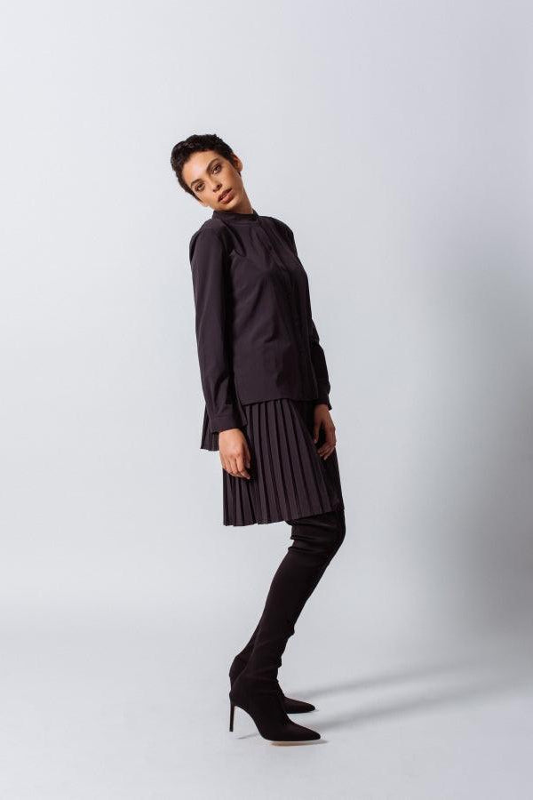 Person wearing a black outfit with a pleated skirt on a white background