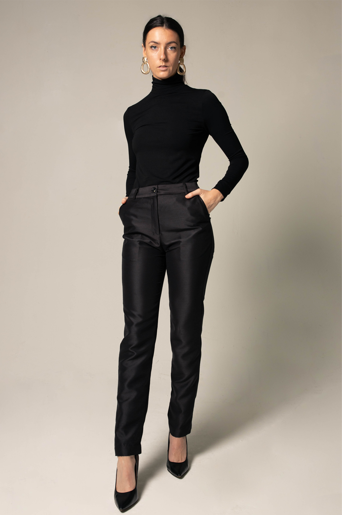 Woman wearing a black turtleneck and black pants against a neutral background