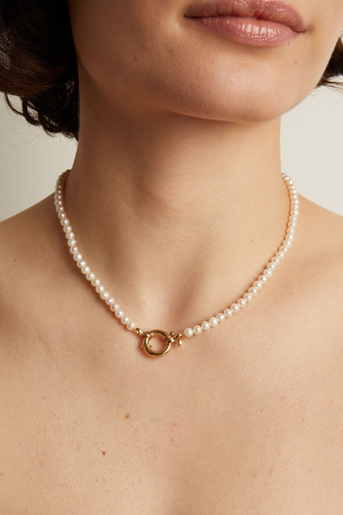 Pearl necklace with a gold clasp worn by a person against a neutral background