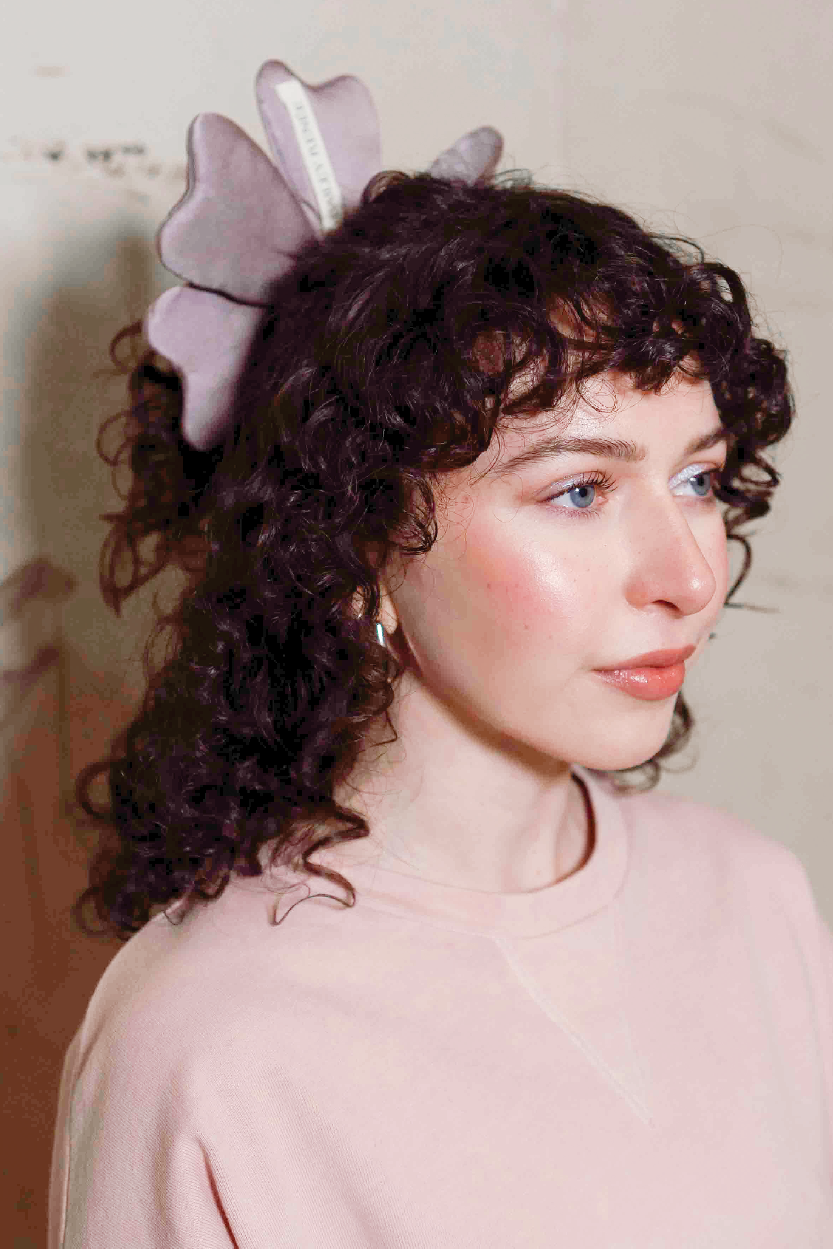 Woman with curly hair wearing a large bow headband against a plain background