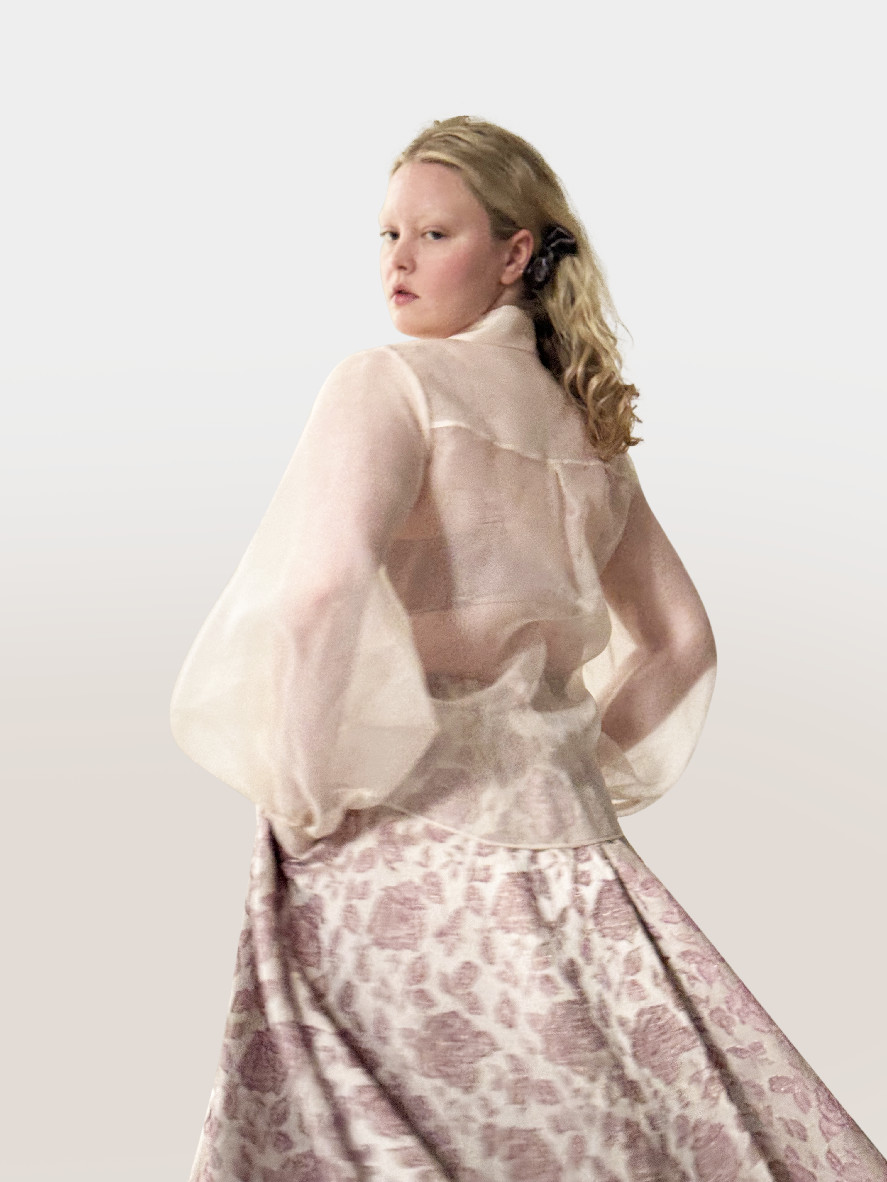 Woman wearing a sheer top and patterned skirt against a white background