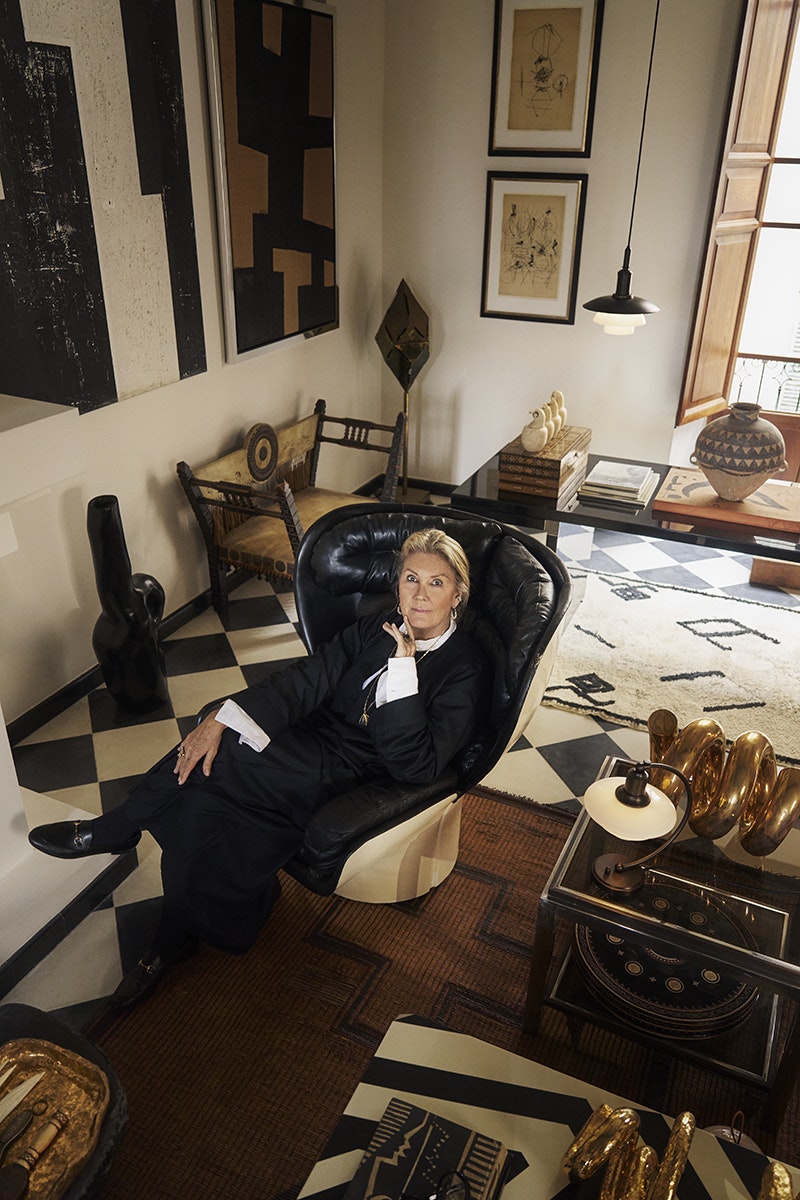 Woman sitting in a stylish chair in an elegant room with geometric patterns and decorative items.