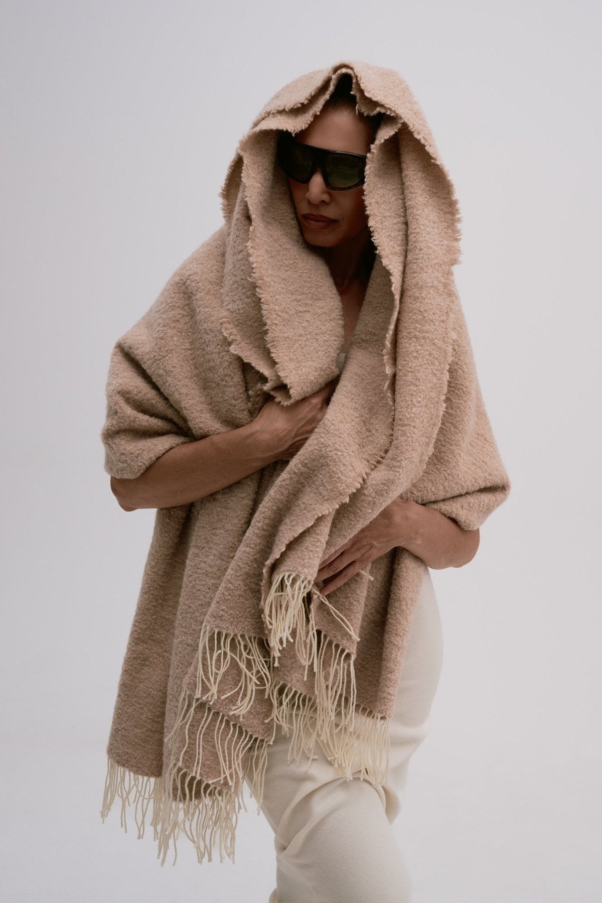 Person wearing a beige blanket as a hood against a plain background
