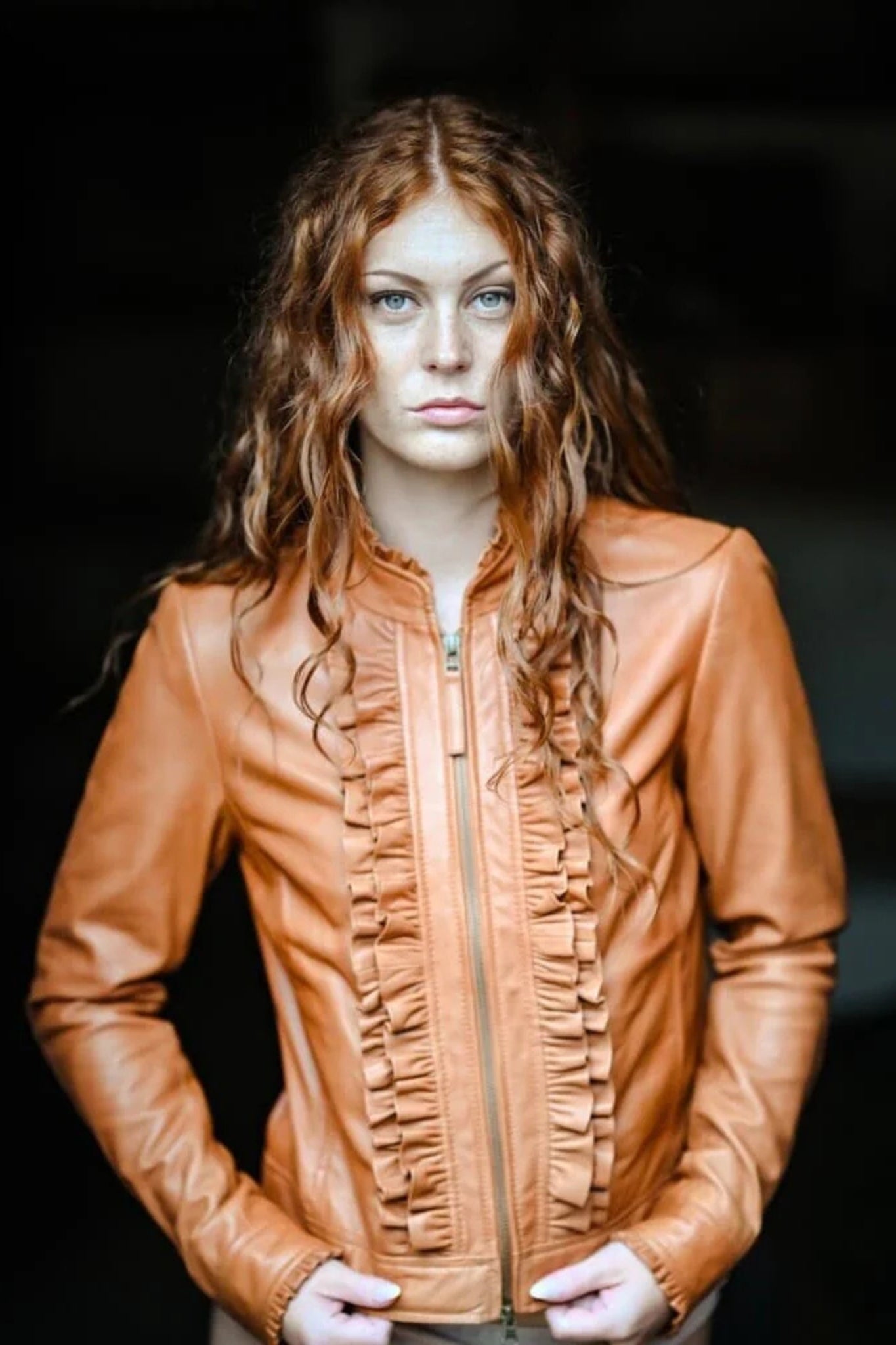 Woman wearing a brown leather jacket against a dark background