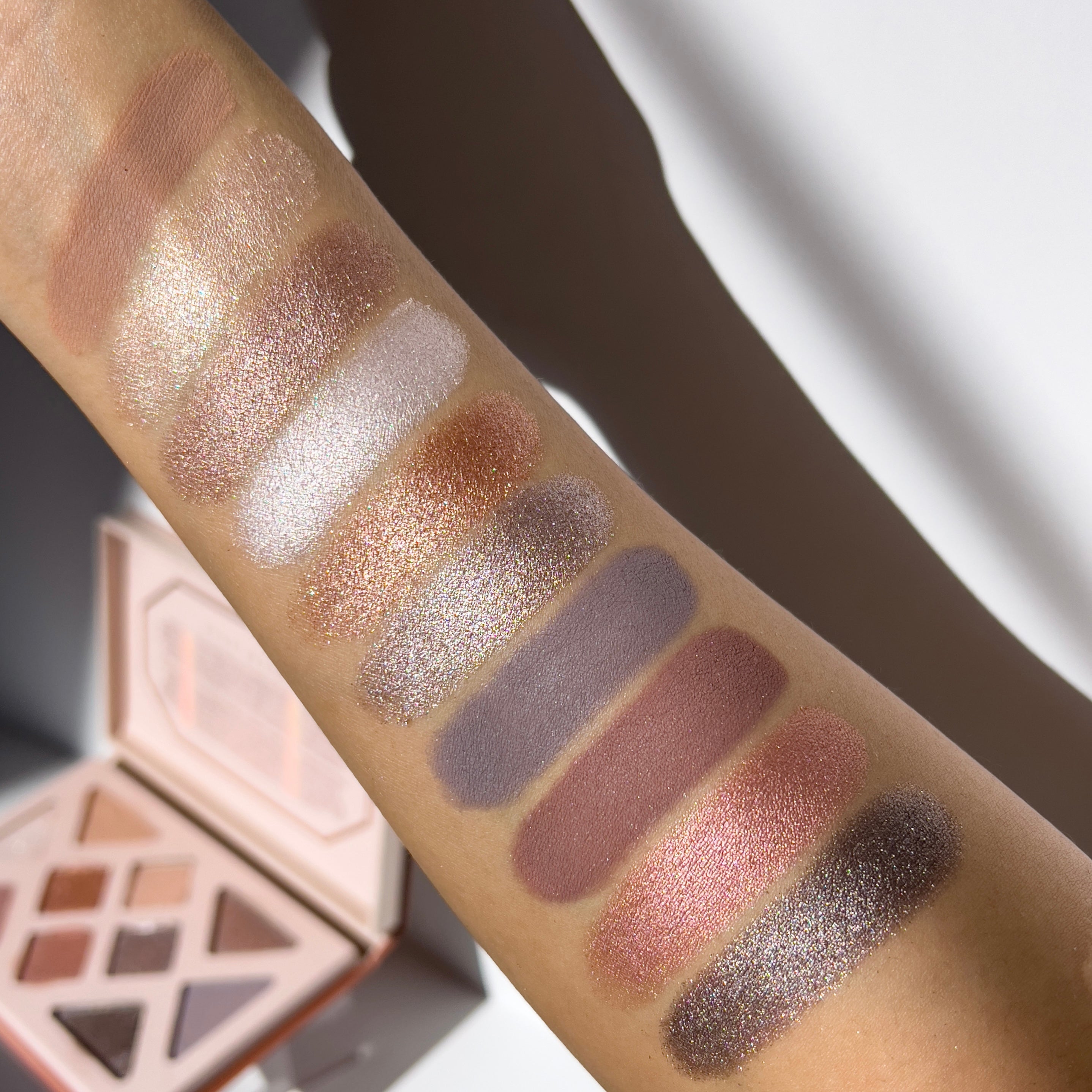 Makeup swatches on a person's arm with a makeup palette in the background