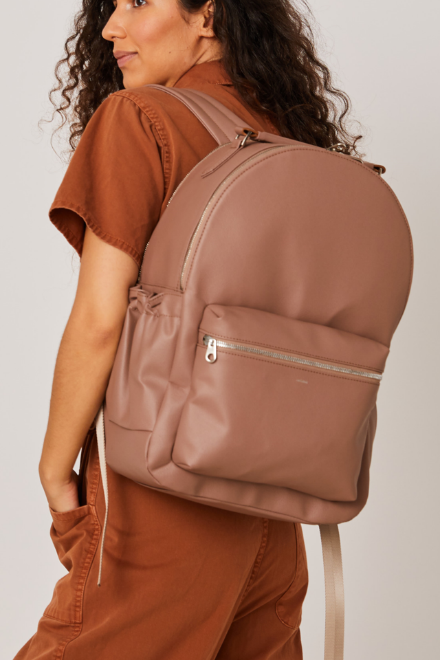 Woman wearing a brown backpack against a plain background