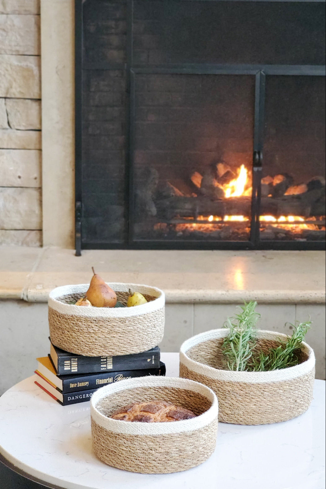 Three woven baskets with plants and books on a table in front of a fireplace.