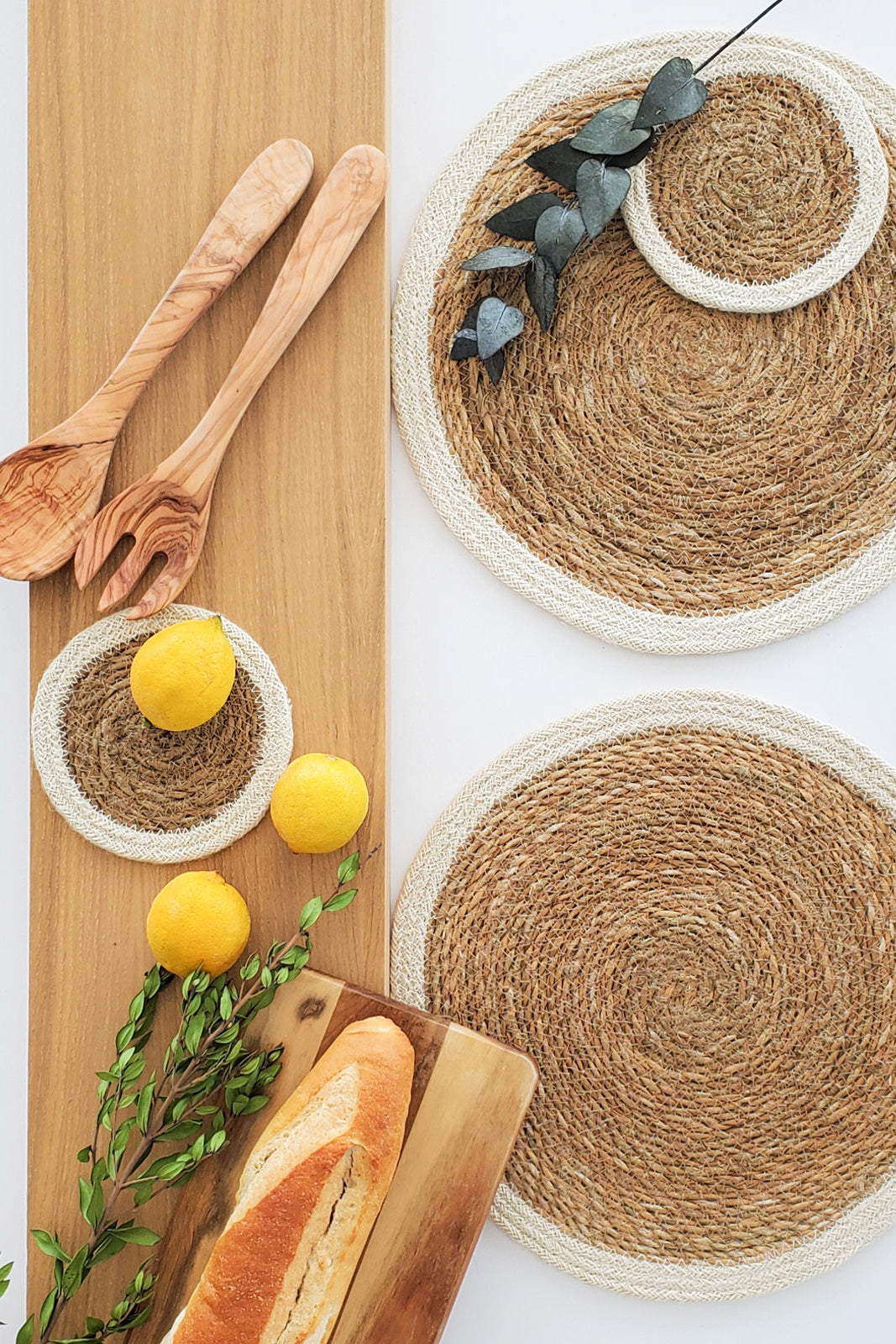 Round woven placemats with wooden utensils and lemons on a wooden board.
