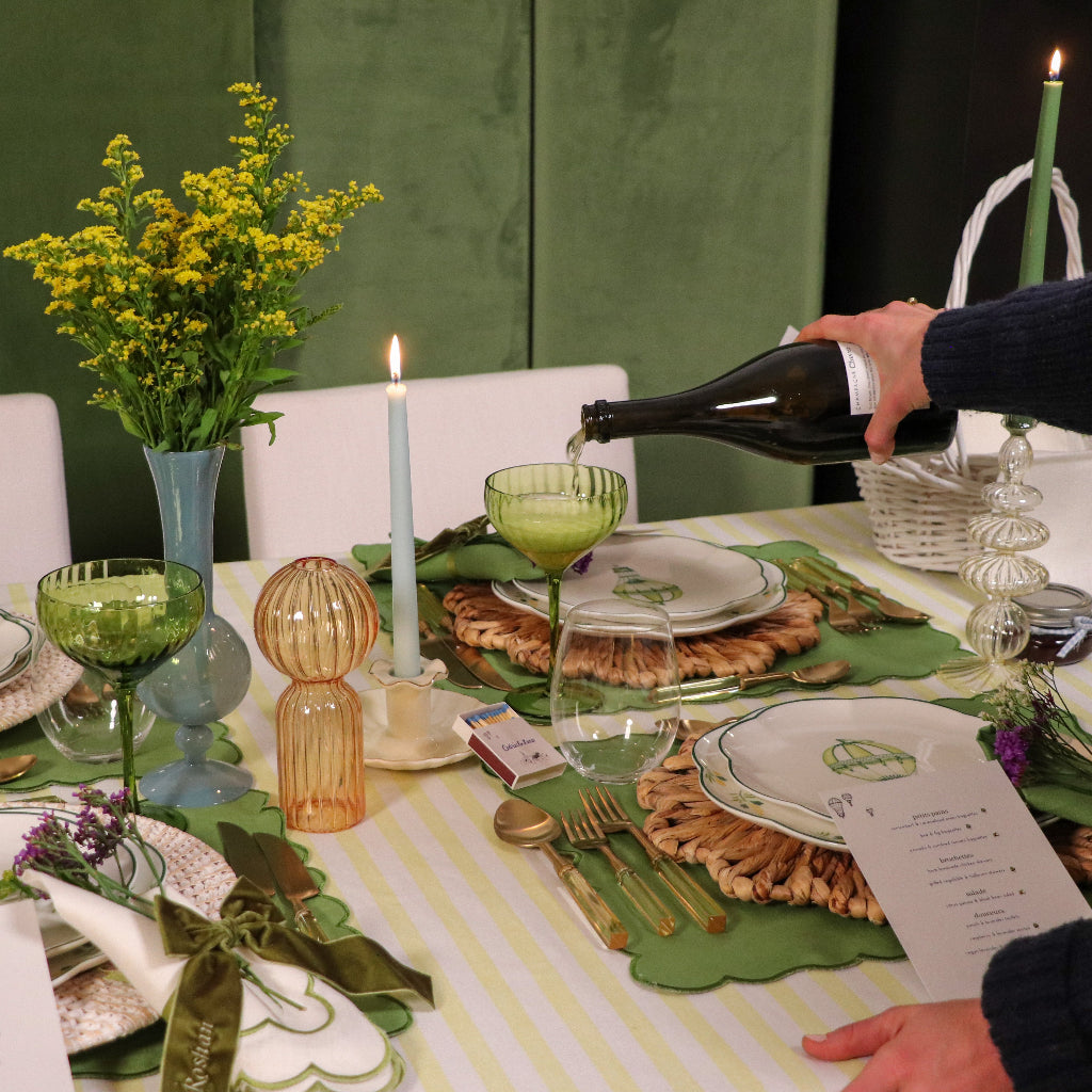 Person pouring wine into a glass at a decorated table with candles and flowers.