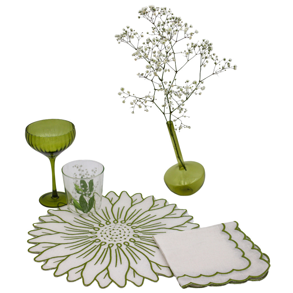 Green glassware and decorative items including a vase with flowers, coasters, and placemats on a white background.